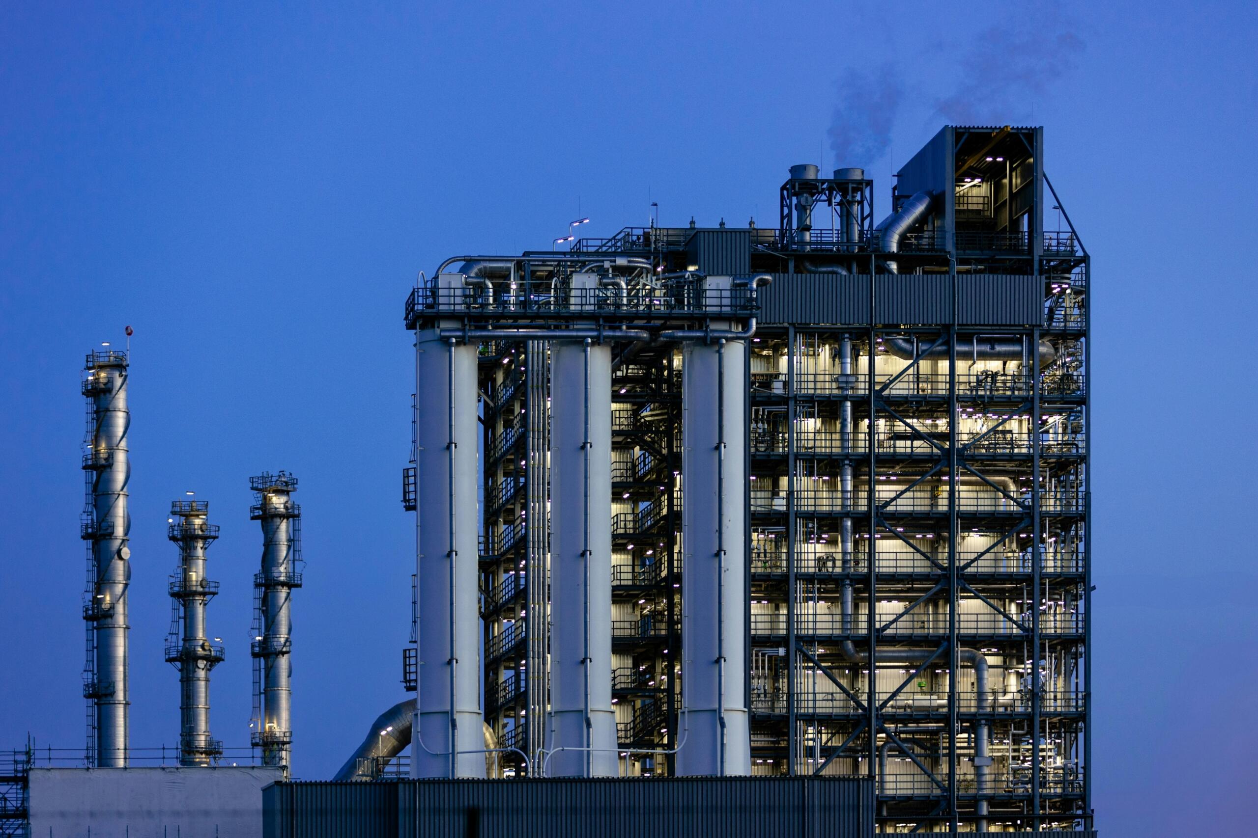 Grote chemische fabriek met verlichte pijpen en installaties bij schemering.
