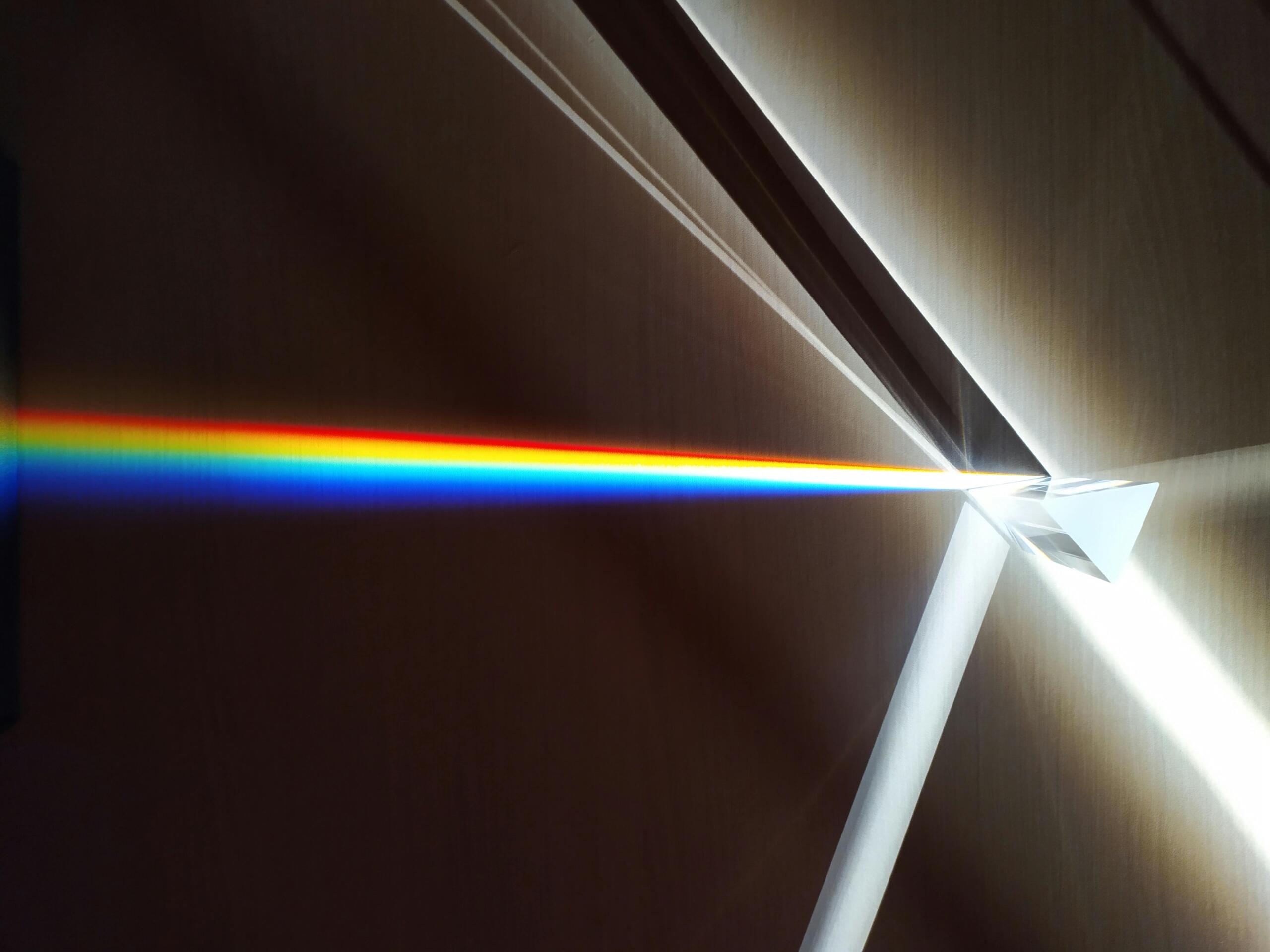 Een glazen prisma breekt een lichtstraal in een spectrale regenboog van kleuren, geprojecteerd op een wand.