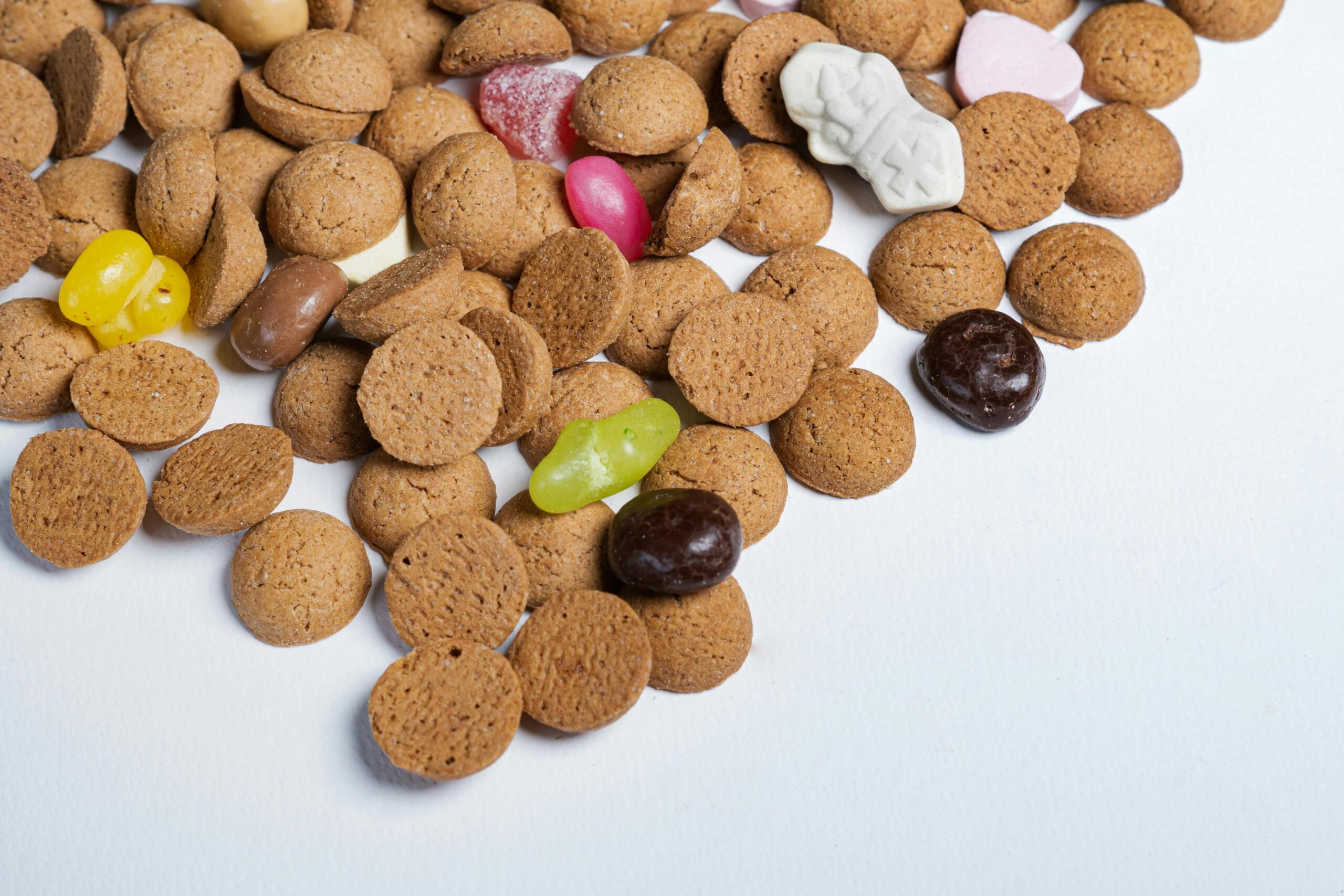 Pepernoten ligt verspreid op een wit oppervlak, met daartussen verschillende gekleurde snoepjes.