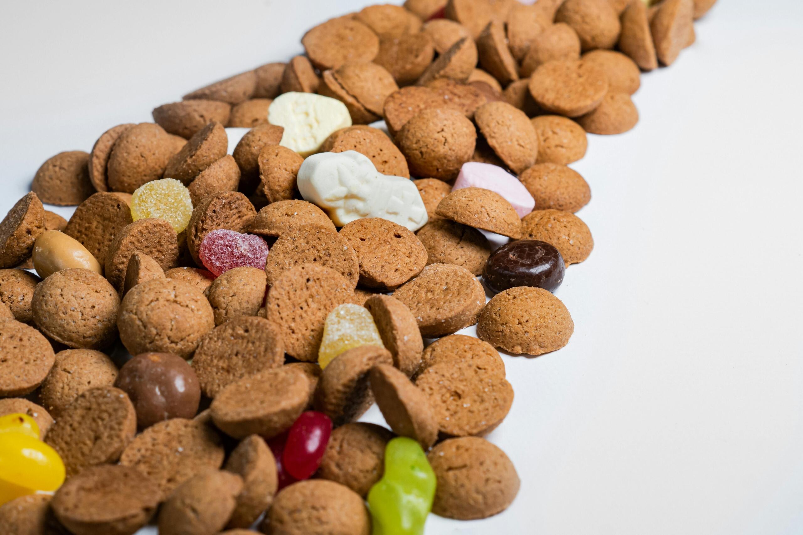 Diagonale strook van kruidnoten met daartussen diverse gekleurde snoepjes op een witte achtergrond.