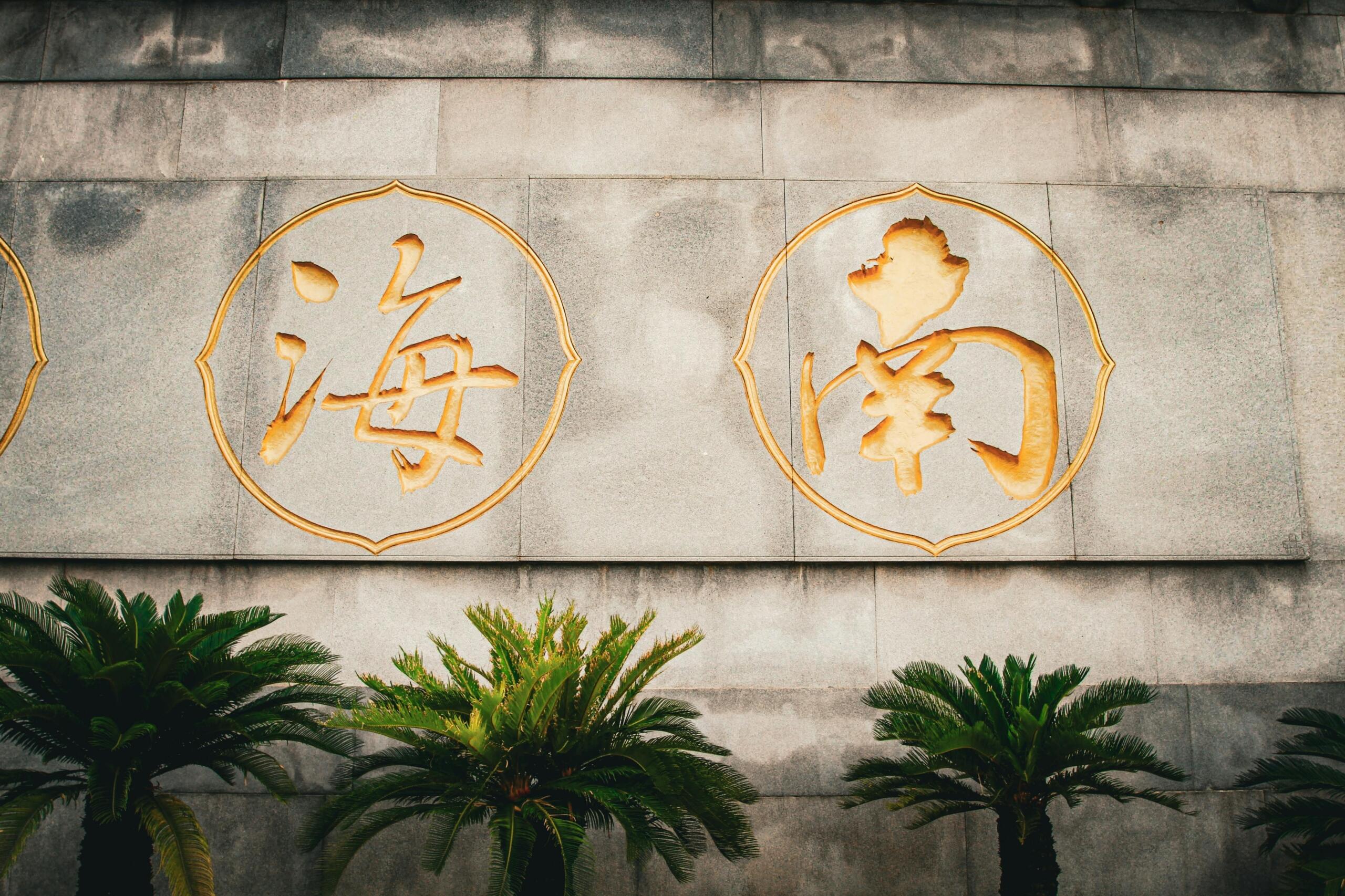 Gouden Chinese karakters gegraveerd op een stenen muur, geflankeerd door palmbomen.