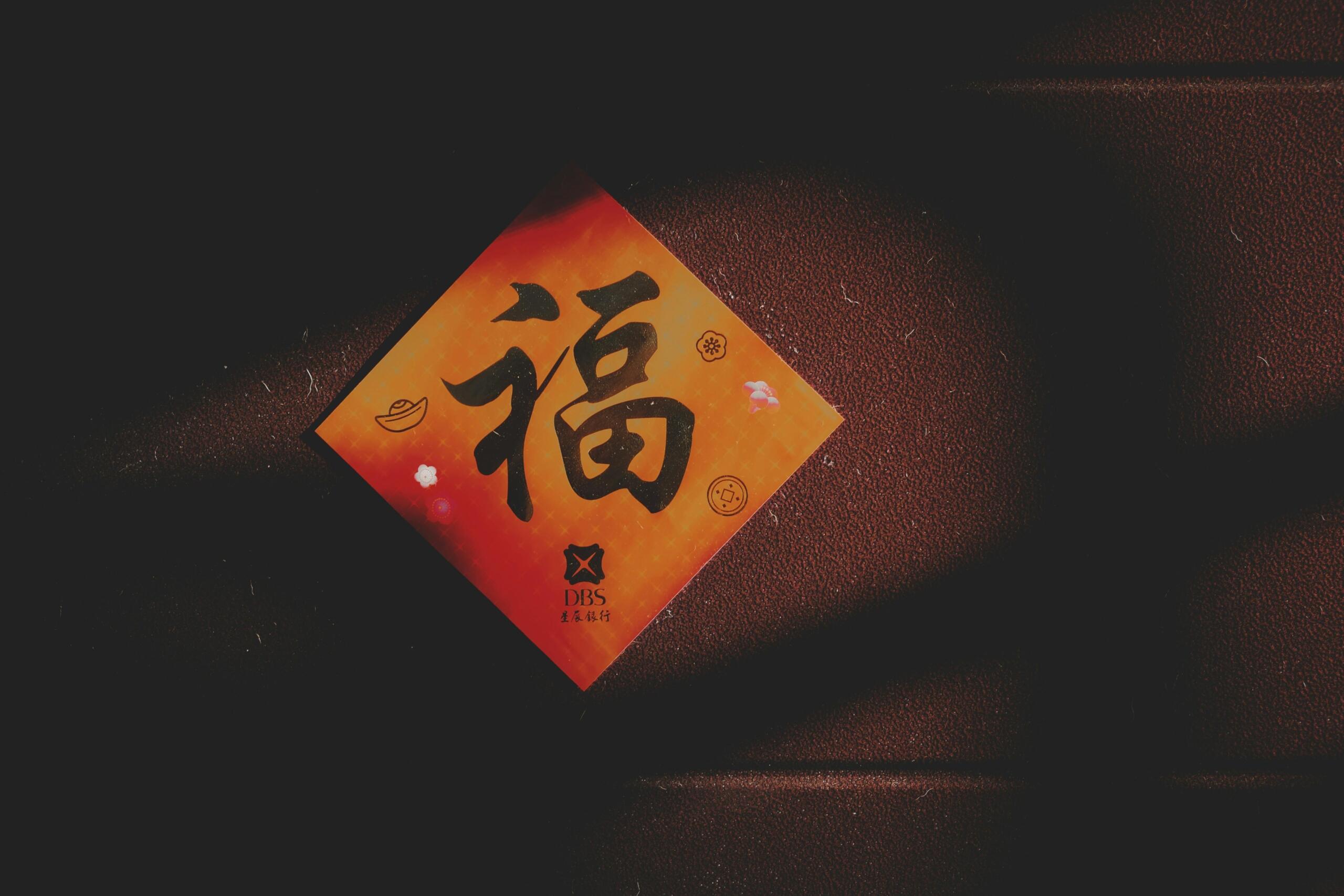Rood-oranje kaart met een groot Chinees teken op een donkere achtergrond, lichtinval creëert schaduw.