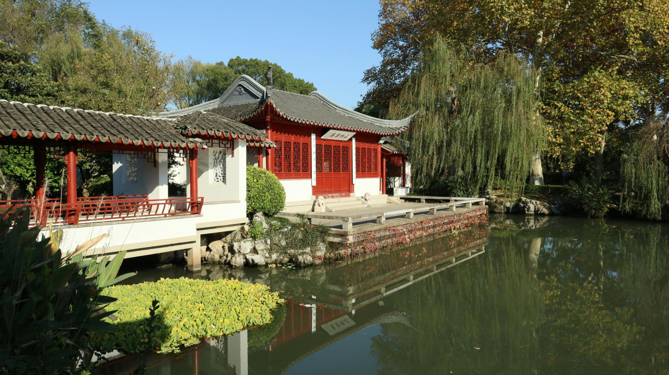 Traditioneel Chinees paviljoen aan de rand van een vijver, tussen groen en stenen elementen.