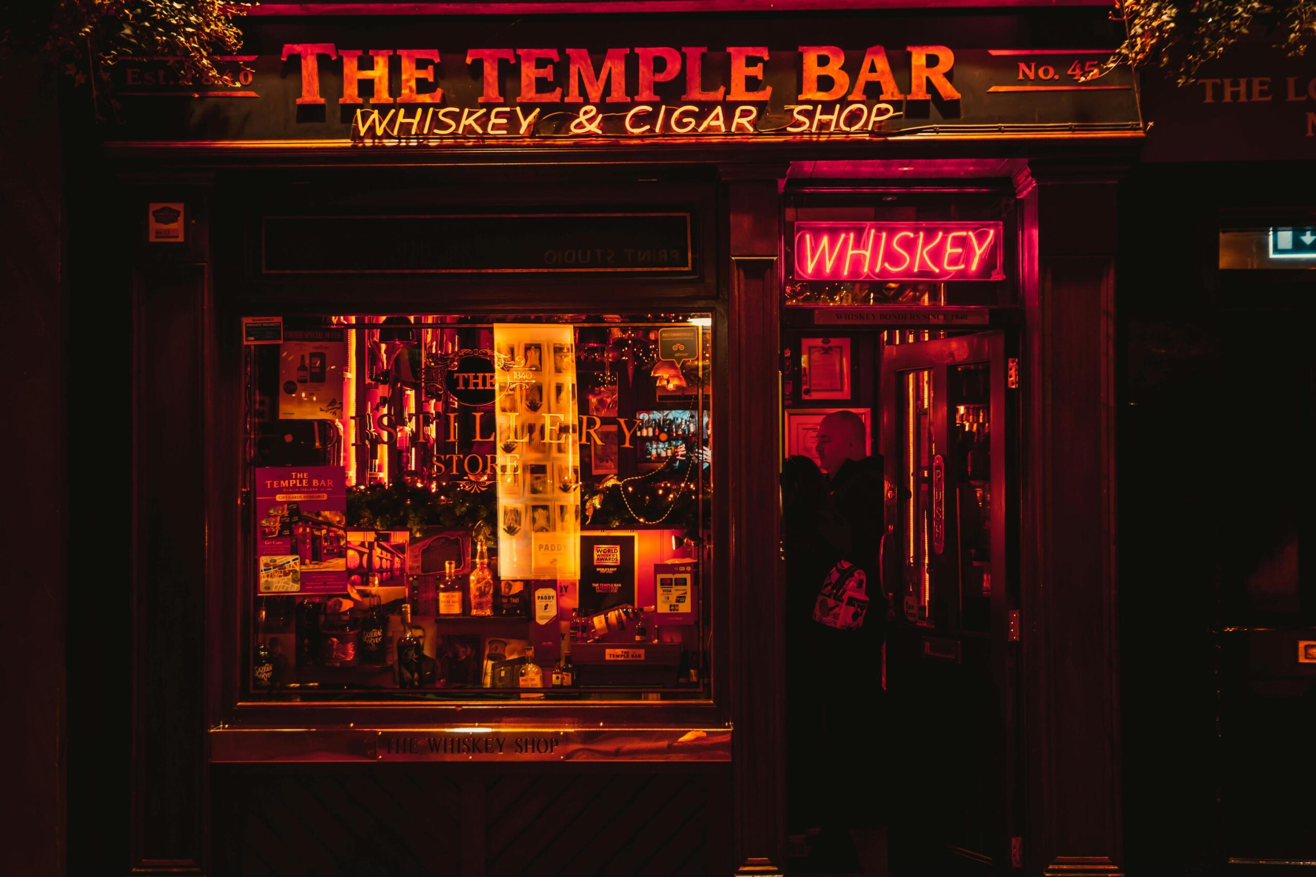 Nachtelijk straatbeeld van de Temple Bar Whiskey & Cigar Shop in Dublin met warm neonlicht.