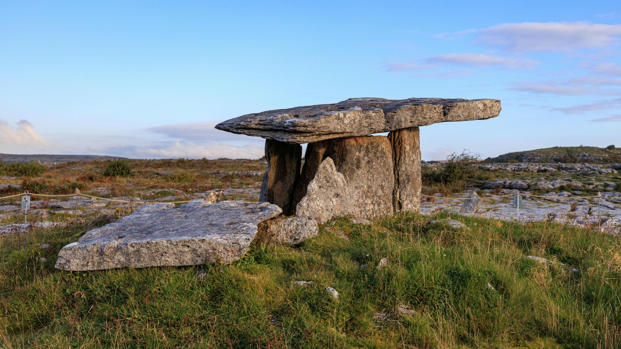 Een prehistorische stenen dolmen in een open, rotsachtig landschap onder een heldere blauwe lucht.