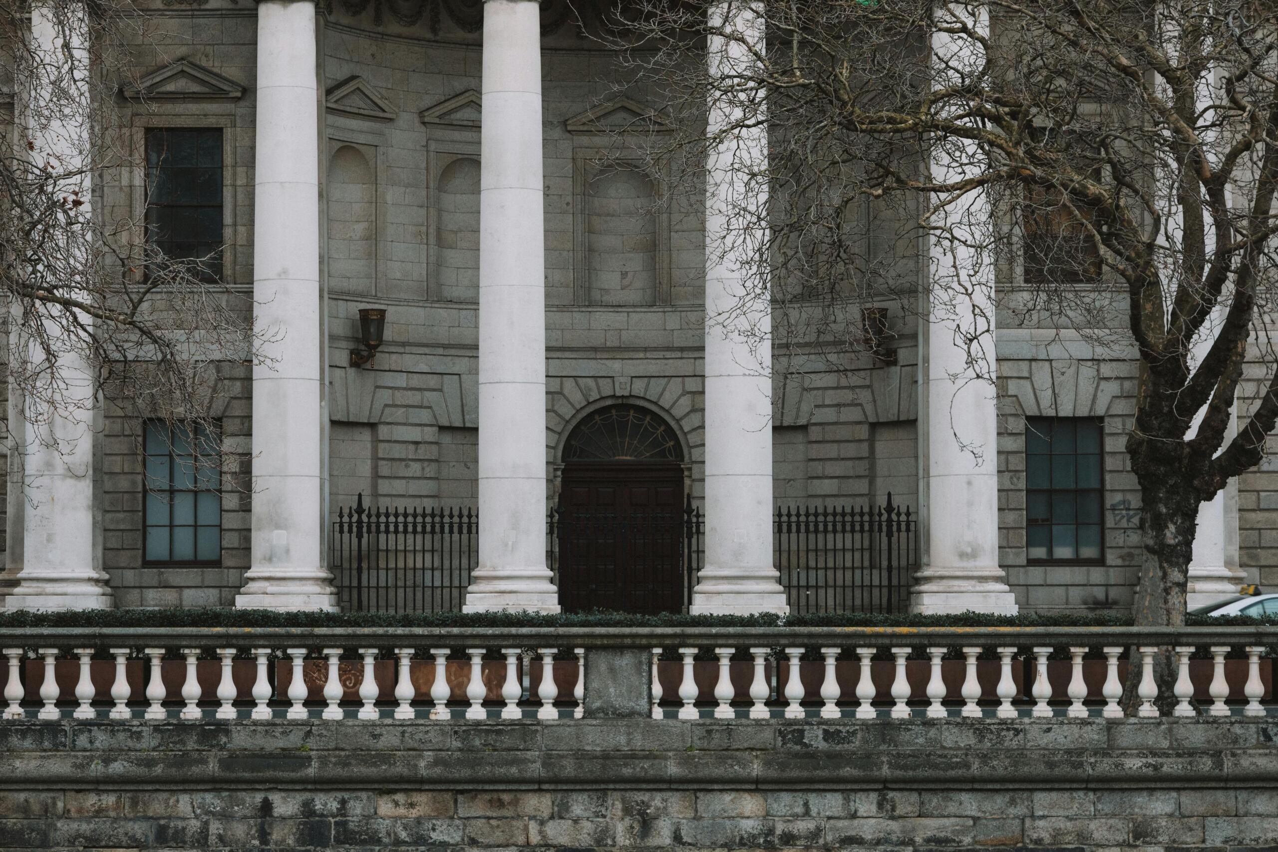 Een imposant stenen gebouw met grote zuilen en klassieke architectuur, geflankeerd door kale bomen.