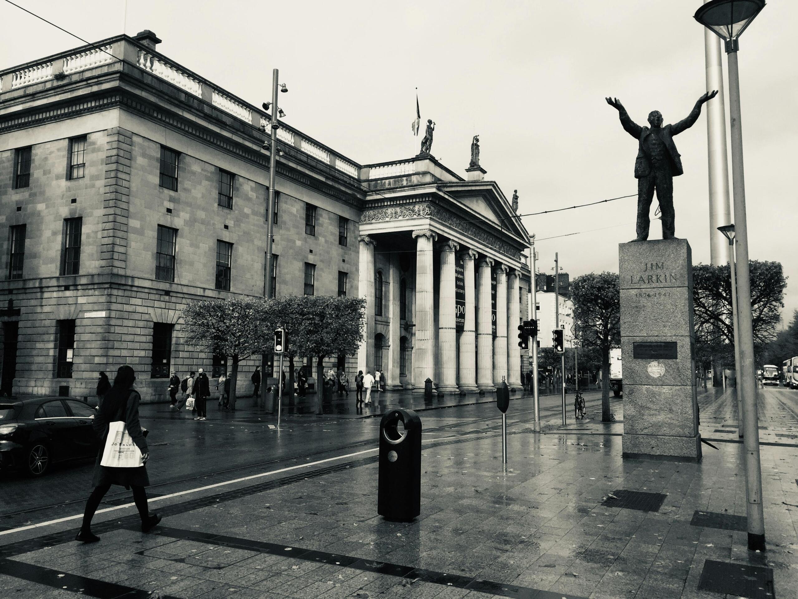 Een zwart-witfoto van een plein in Dublin met een standbeeld van vakbondsleider Jim Larkin voor een gebouw met klassieke zuilen.