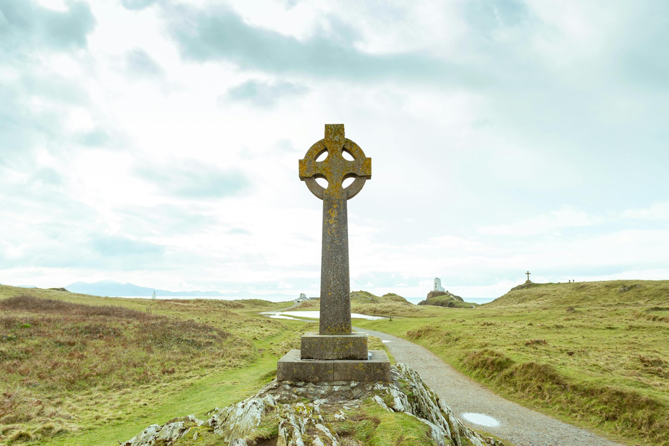 Een groot Keltisch kruis staat op een rotsachtig plateau te midden van een golvend, open landschap met wandelpaden.