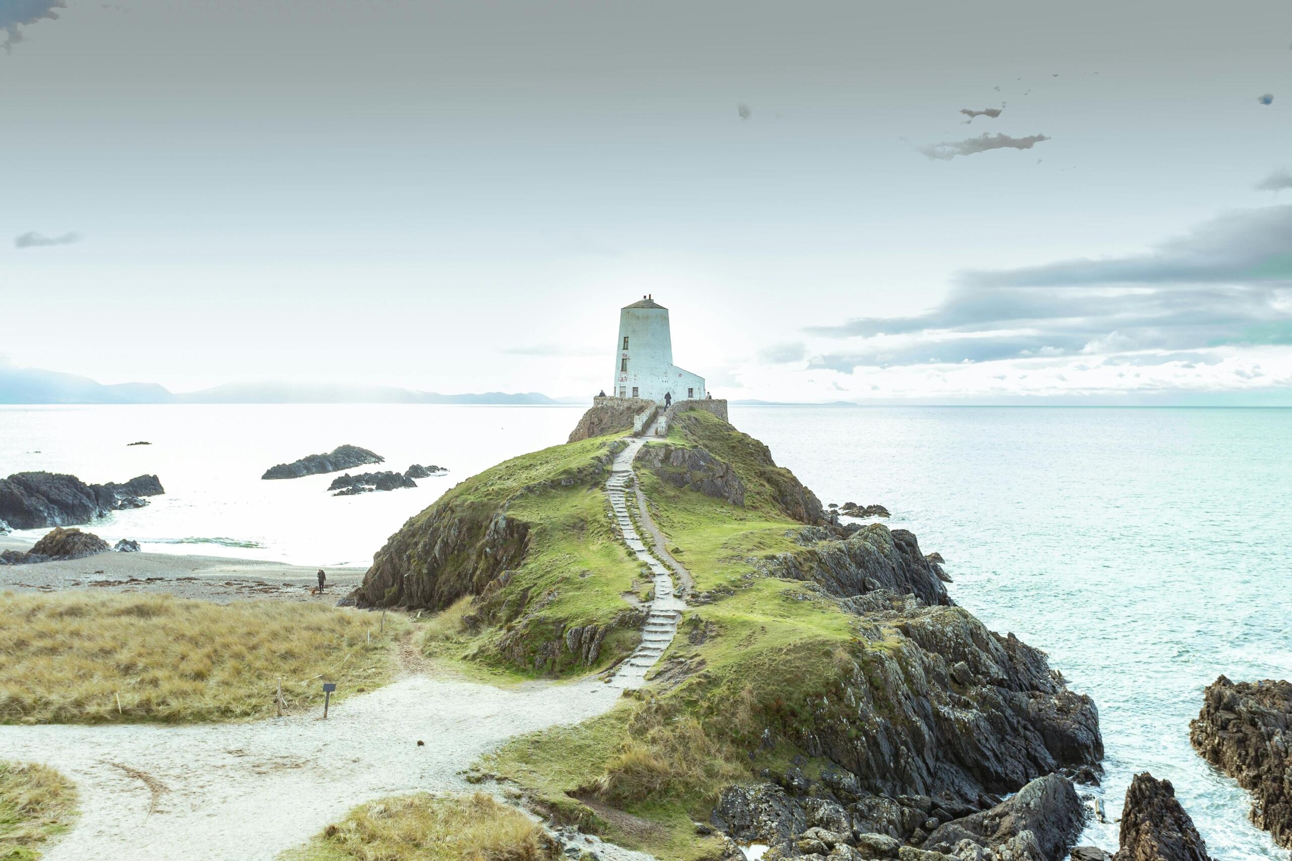 Een lang pad dat omhoog loopt naar een witte kusttoren, omringd door rotsen en de zee.