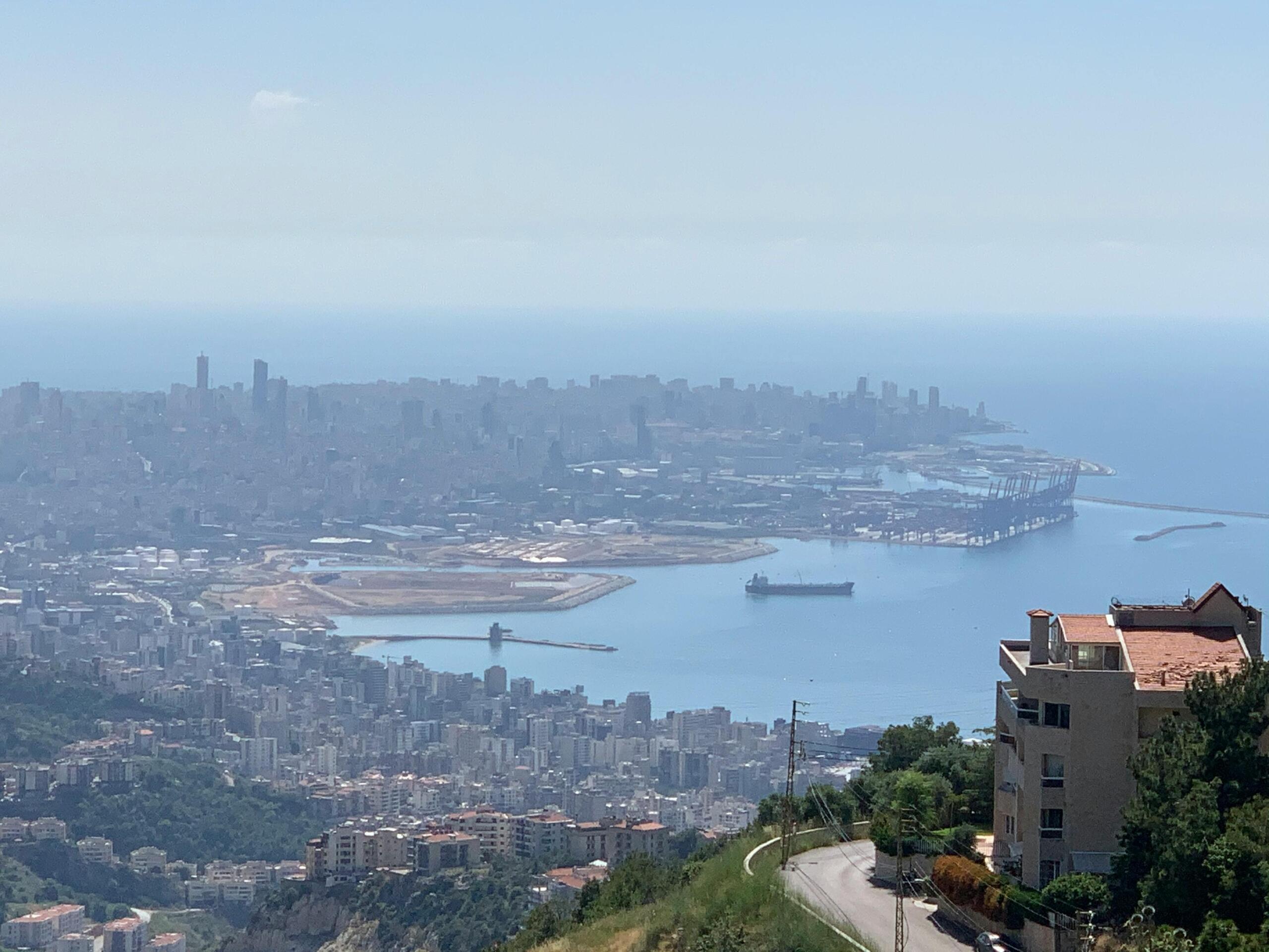 Panoramisch uitzicht over Beiroet met de haven, laadkranen, schepen en dichtbebouwde stadsblokken die uitkomen op de Middellandse Zee.