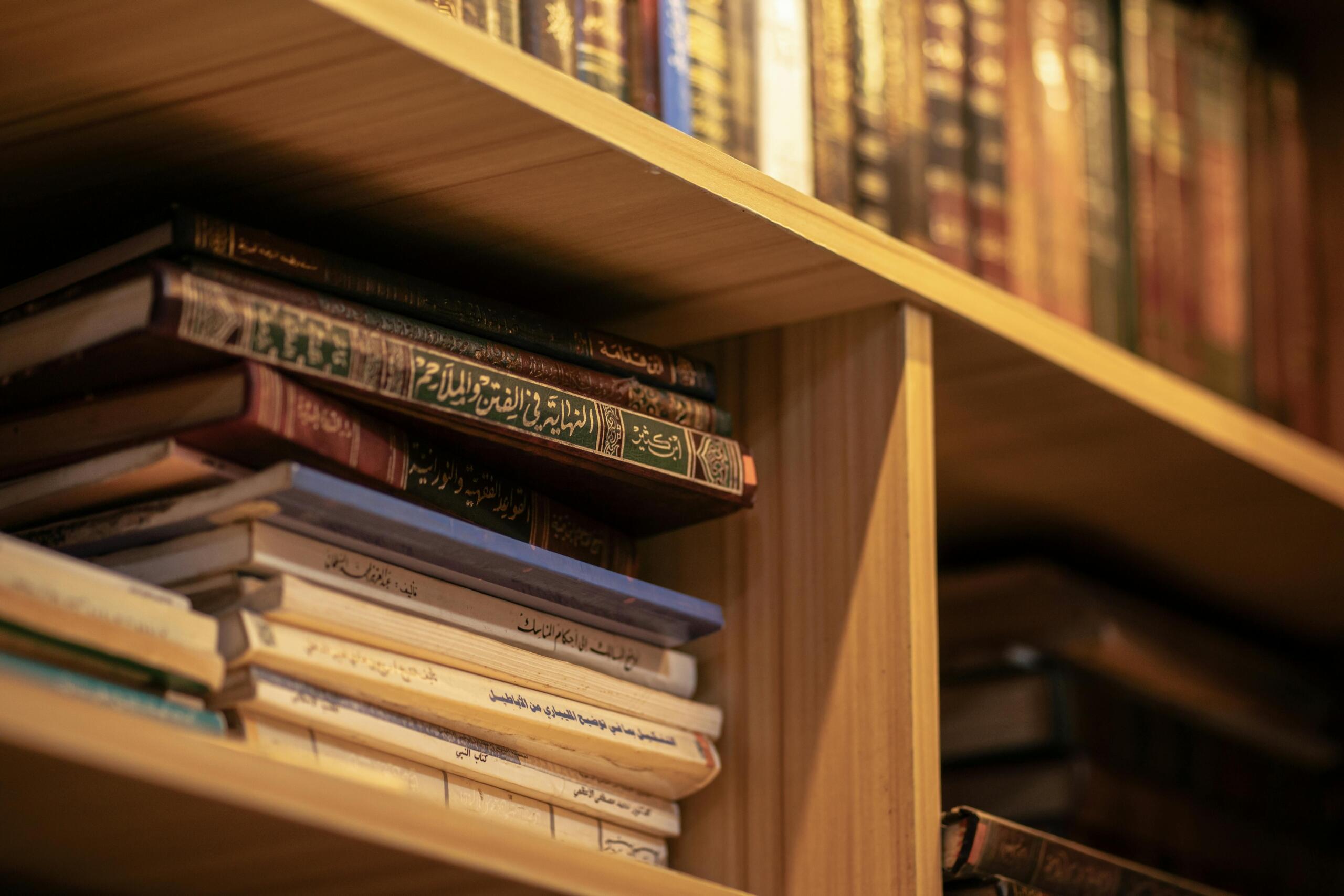 Een stapel versleten islamitische en Arabische boeken ligt op een houten plank, met ruggen die zijn versierd met sierlijk schrift in goud en groen.