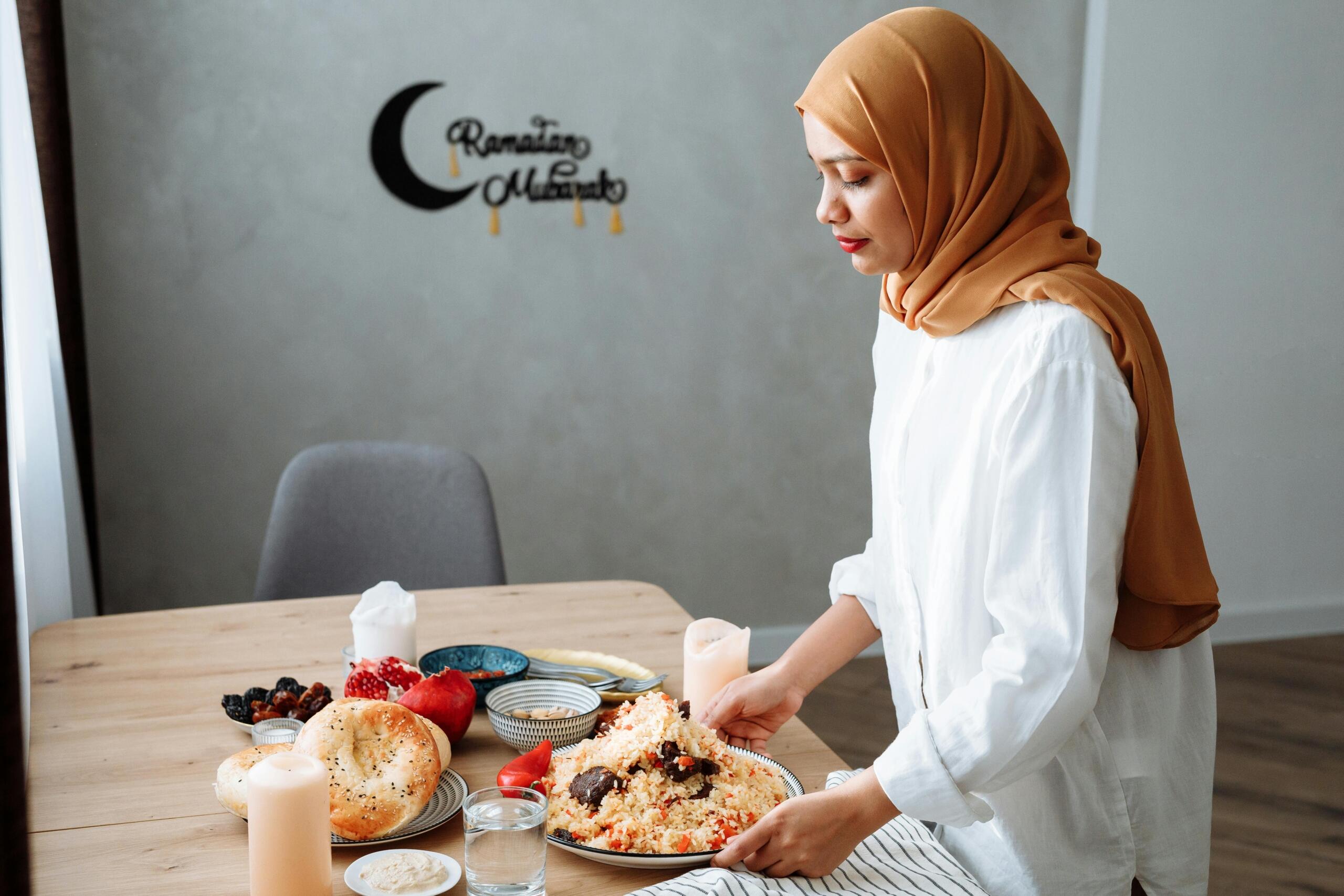 Een jonge moslima met een hijab zet kommen met rijst, brood en fruit op een tafel die is versierd voor de Ramadan.