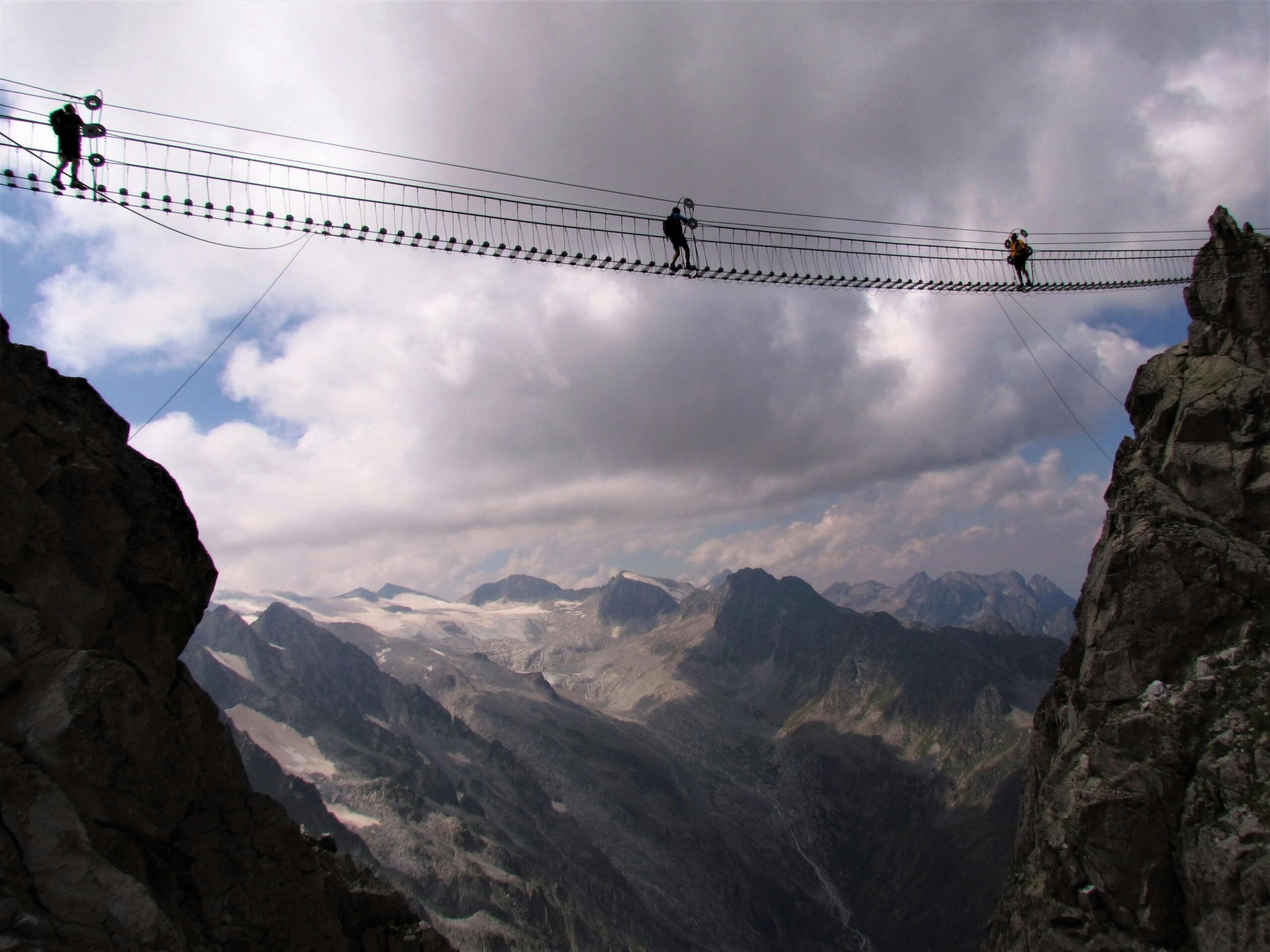 Mensen steken een touwhangbrug over tussen rotsen hoog boven een bergdal
