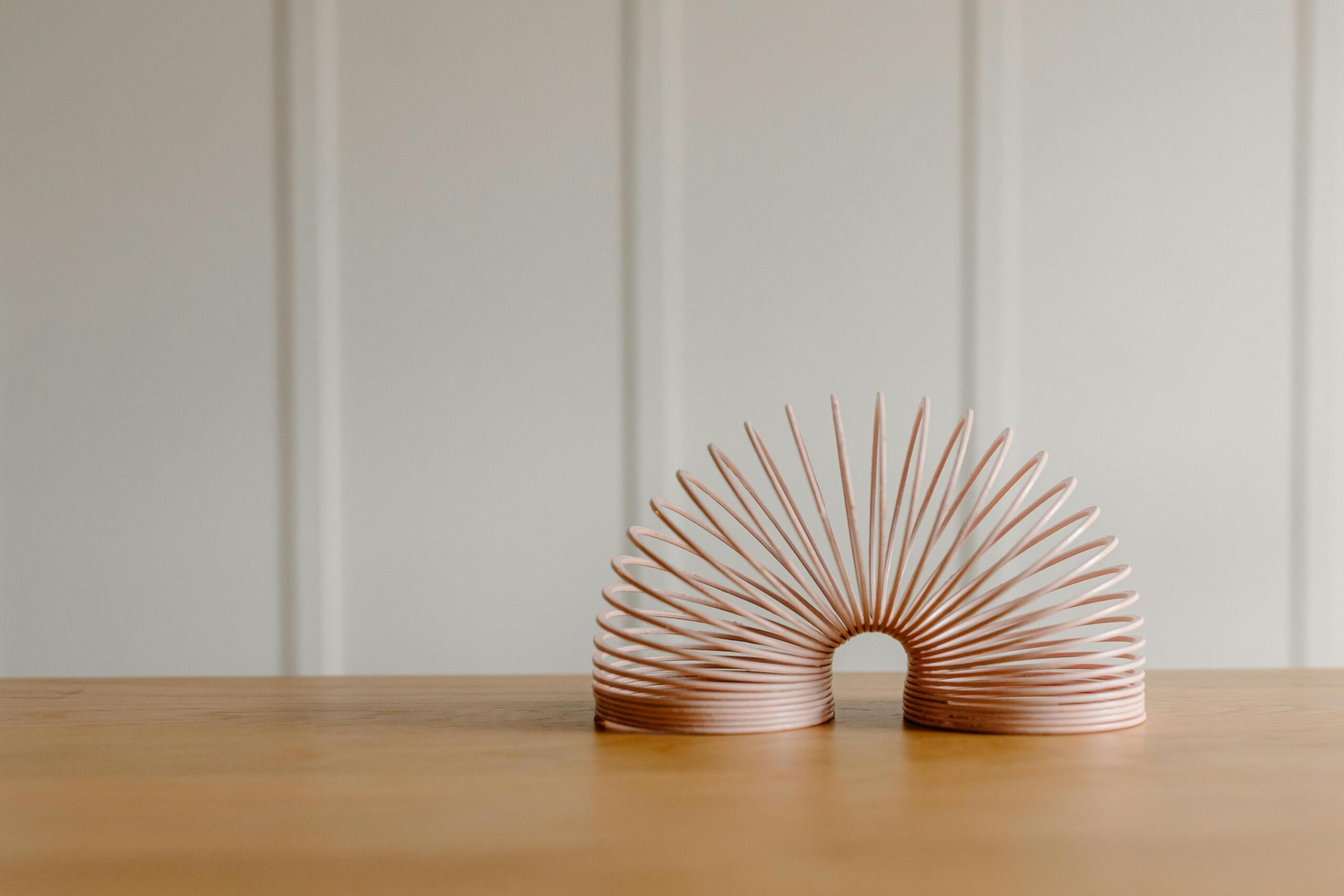 Roze slinky in een boog op een houten tafel, met focus op de spiralen.