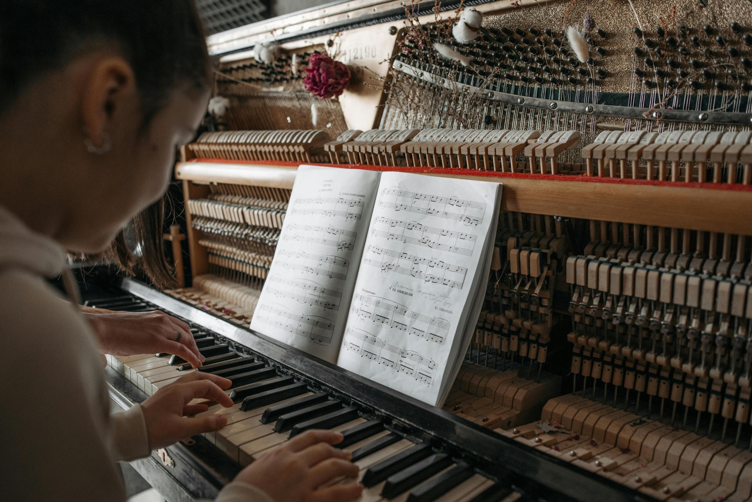 Persoon bespeelt een piano met open binnenwerk, met bladmuziek op de standaard.