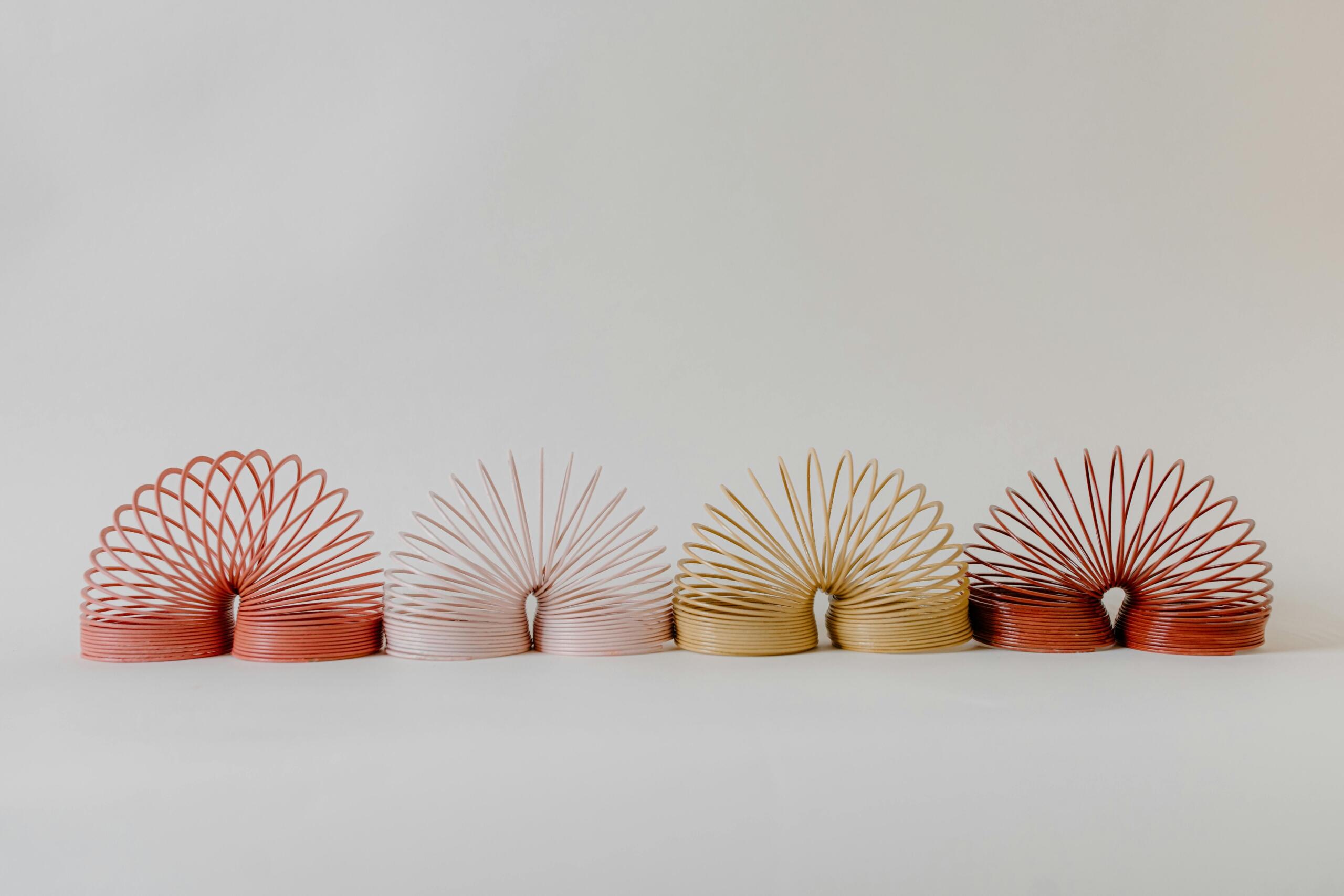 Vier kleurrijke slinky’s staan in een boog op een witte ondergrond.