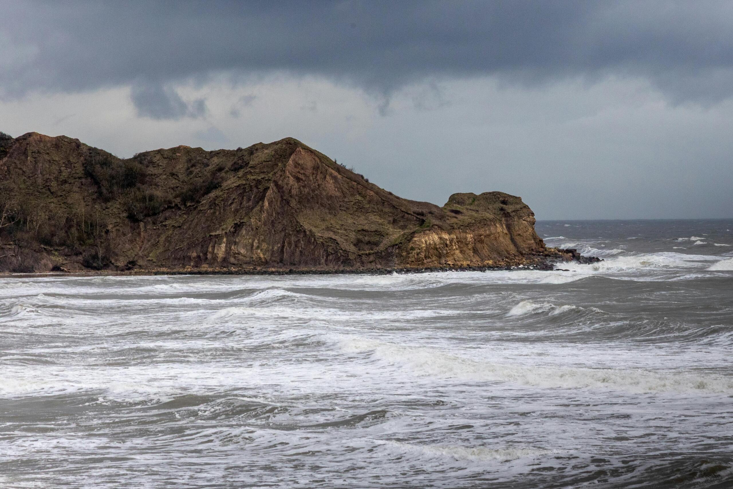 Golven van de zee komen binnen aan de kust, met gebergte op de achtergrond.