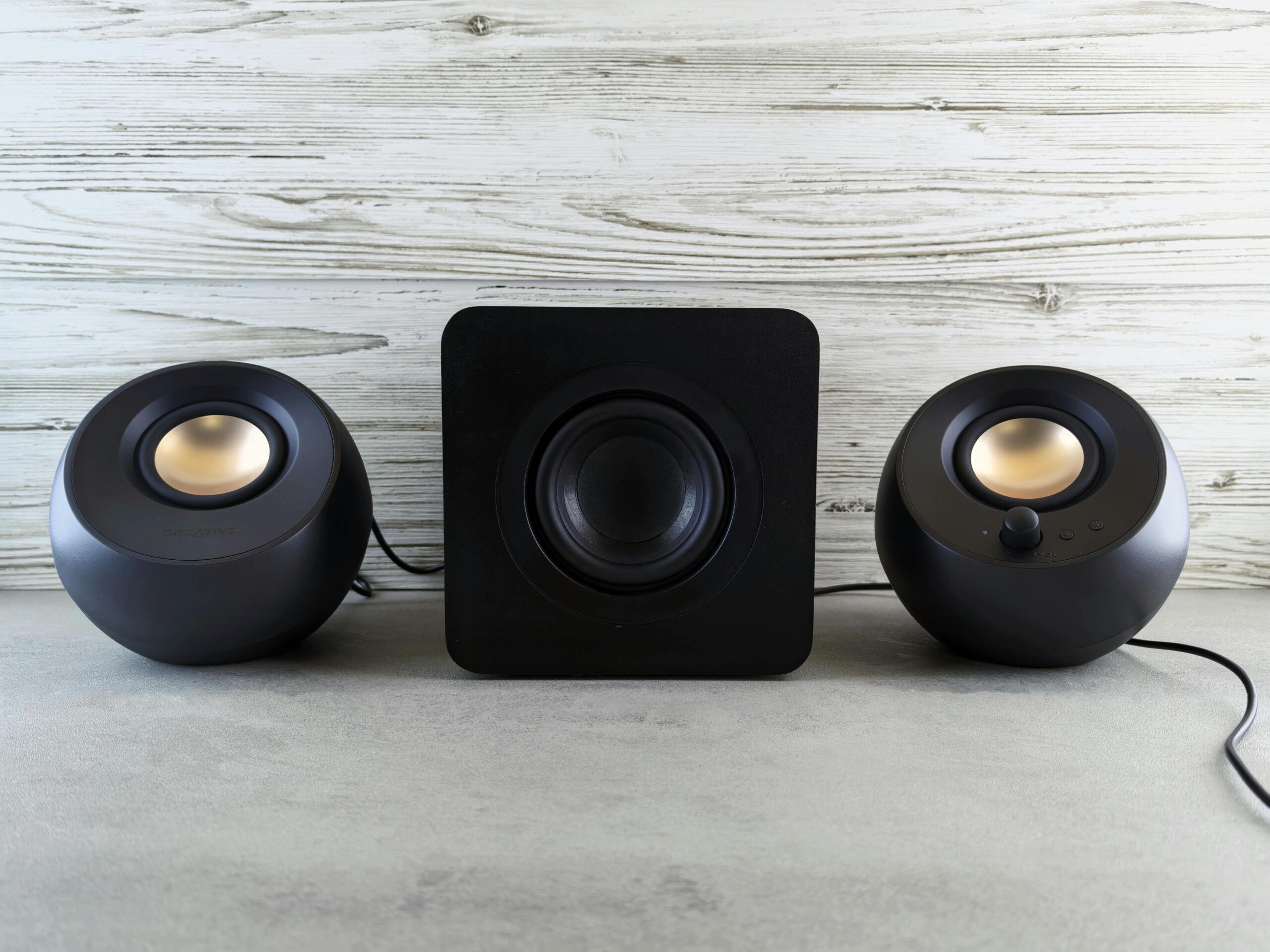 Zwart speakerset met twee ronde satellieten en een centrale subwoofer staat op een houten oppervlak.