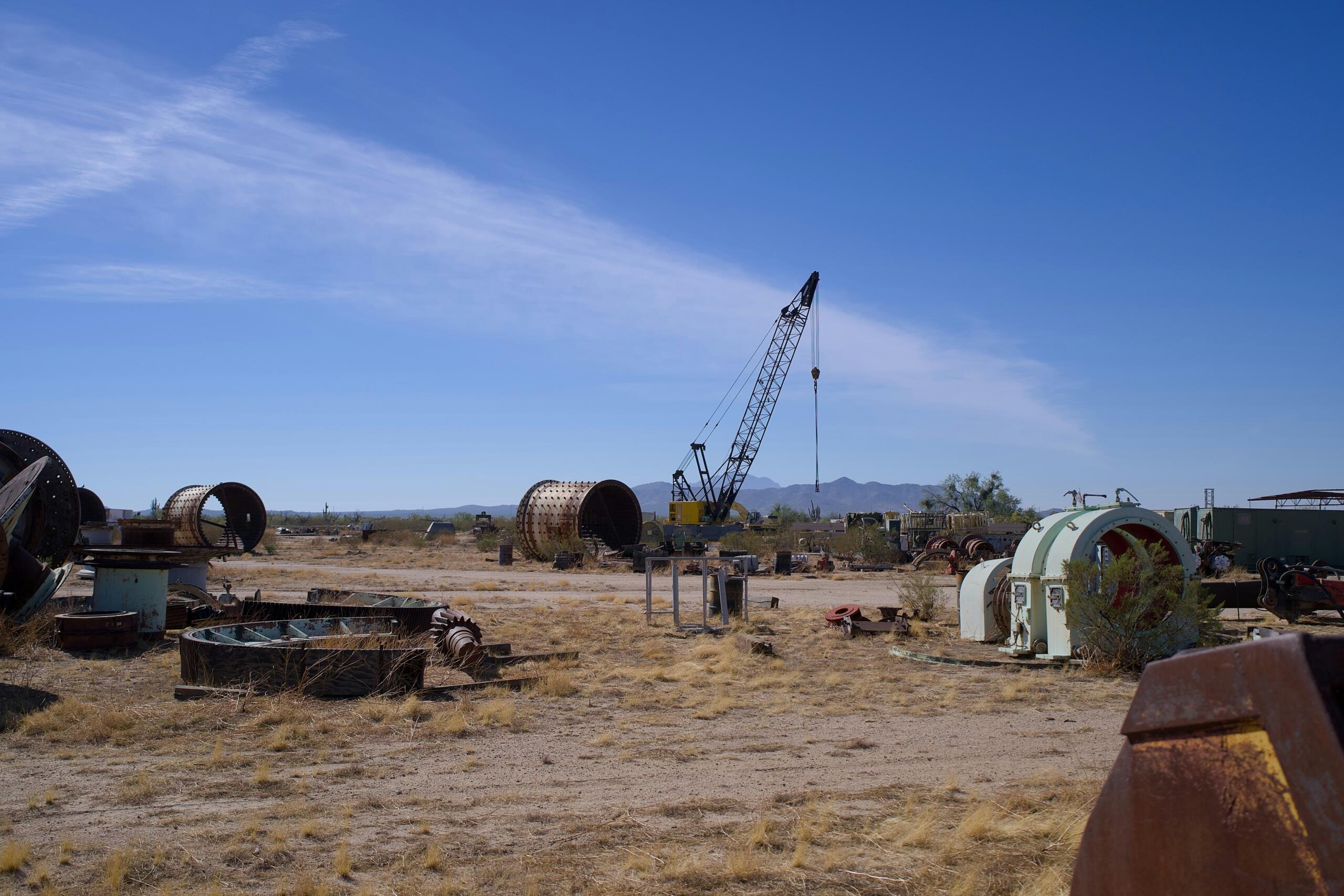 Een schrootwerf met een kraan en zware industriële machines onder een heldere blauwe lucht.