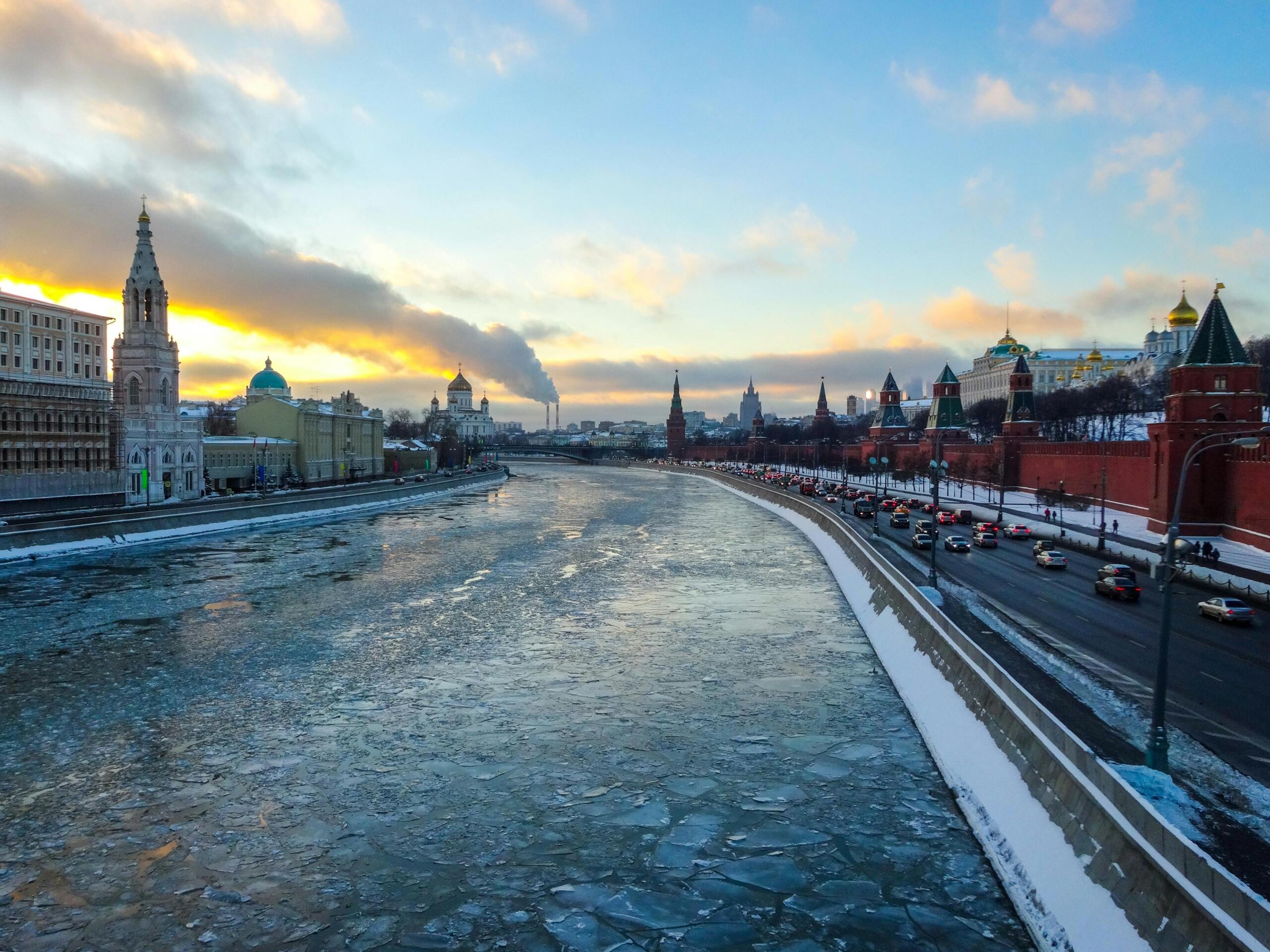 Een panorama van de bevroren Moskva‑rivier bij zonsondergang met aan weerszijden de torens en muren van het Kremlin en de kleurrijke koepels.