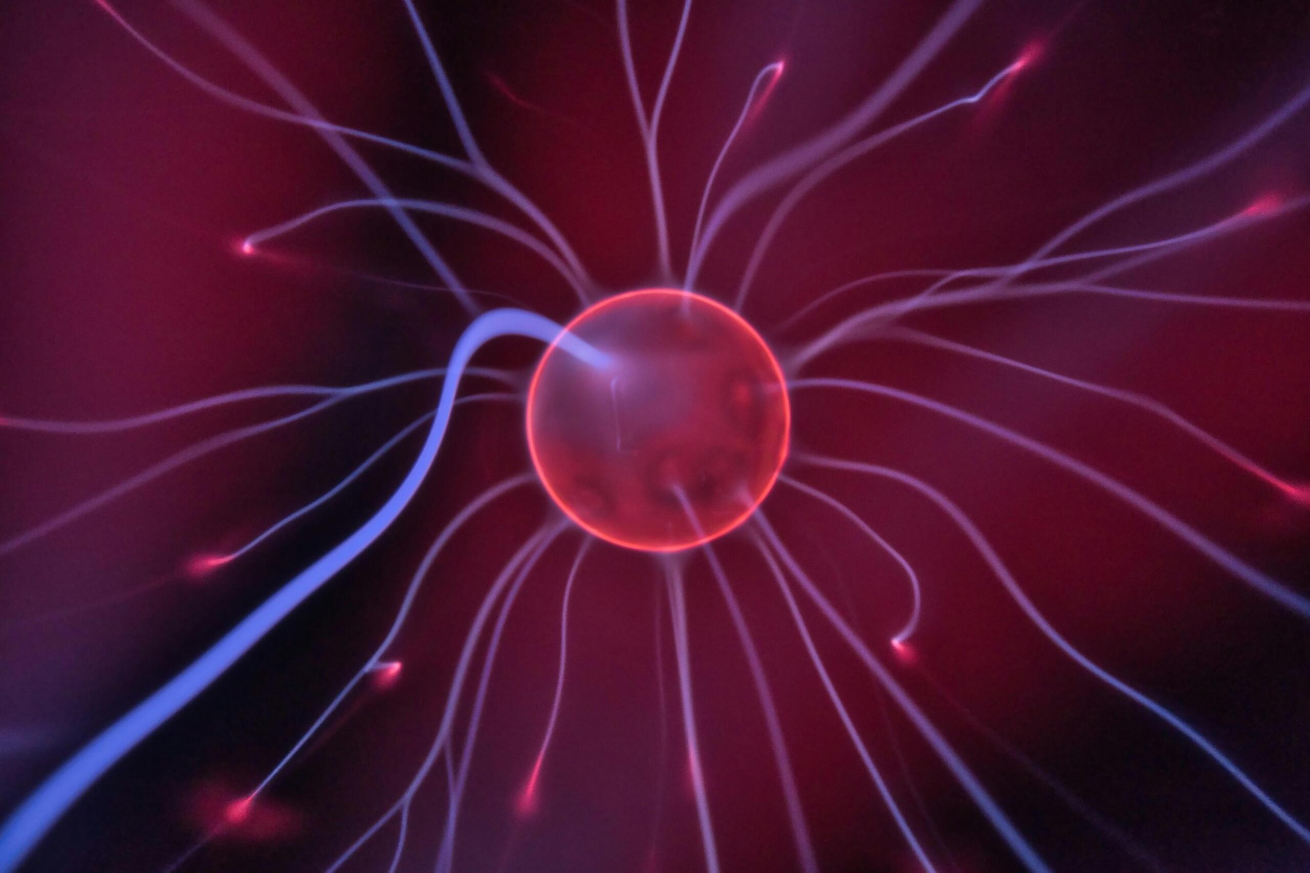 Een close‑up van een plasmabol waarin kleurrijke elektrische stromen naar buiten lopen en gloeiende filamenten vormen.