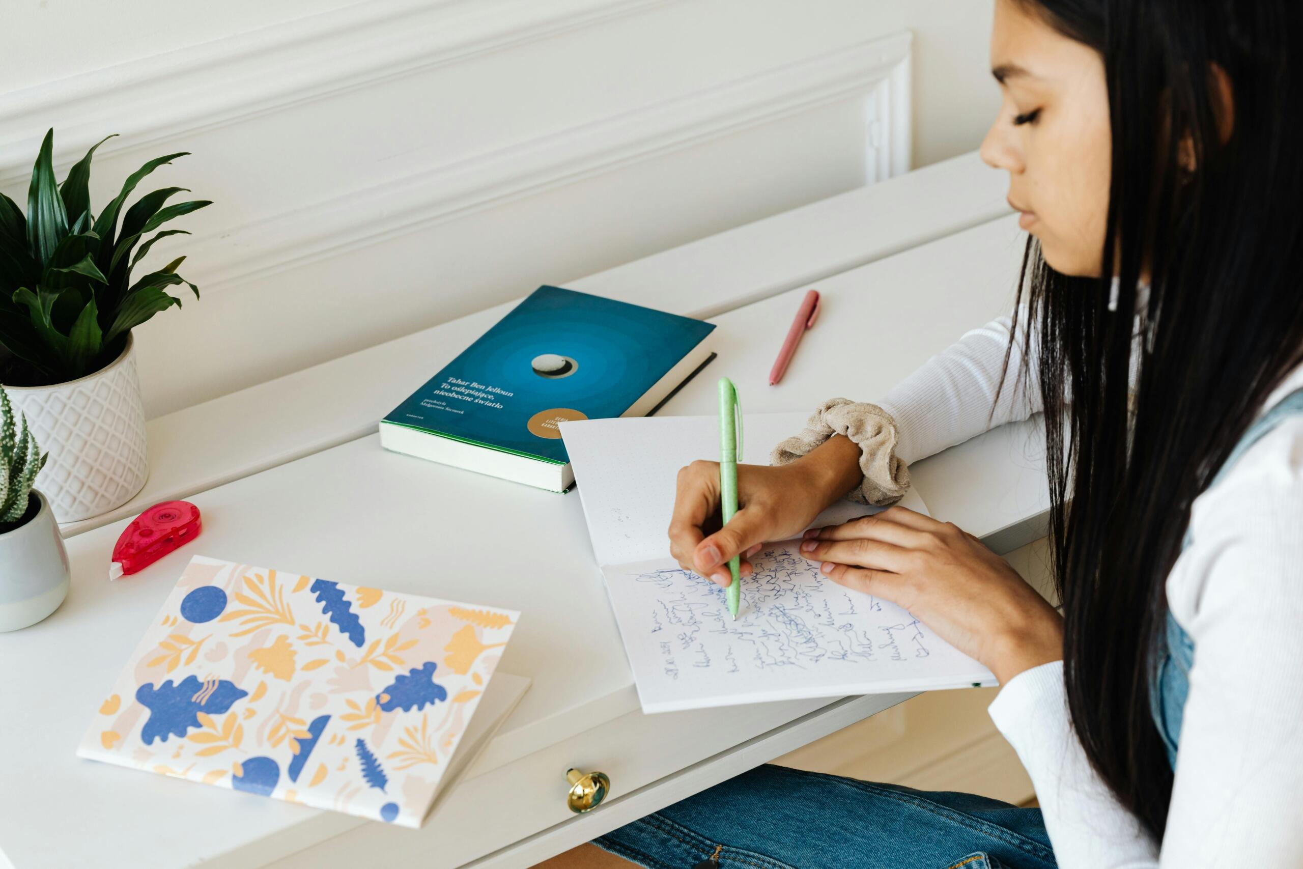Een jonge studente schrijft geconcentreerd in haar notitieboek aan een bureau met schoolspullen en een plant.