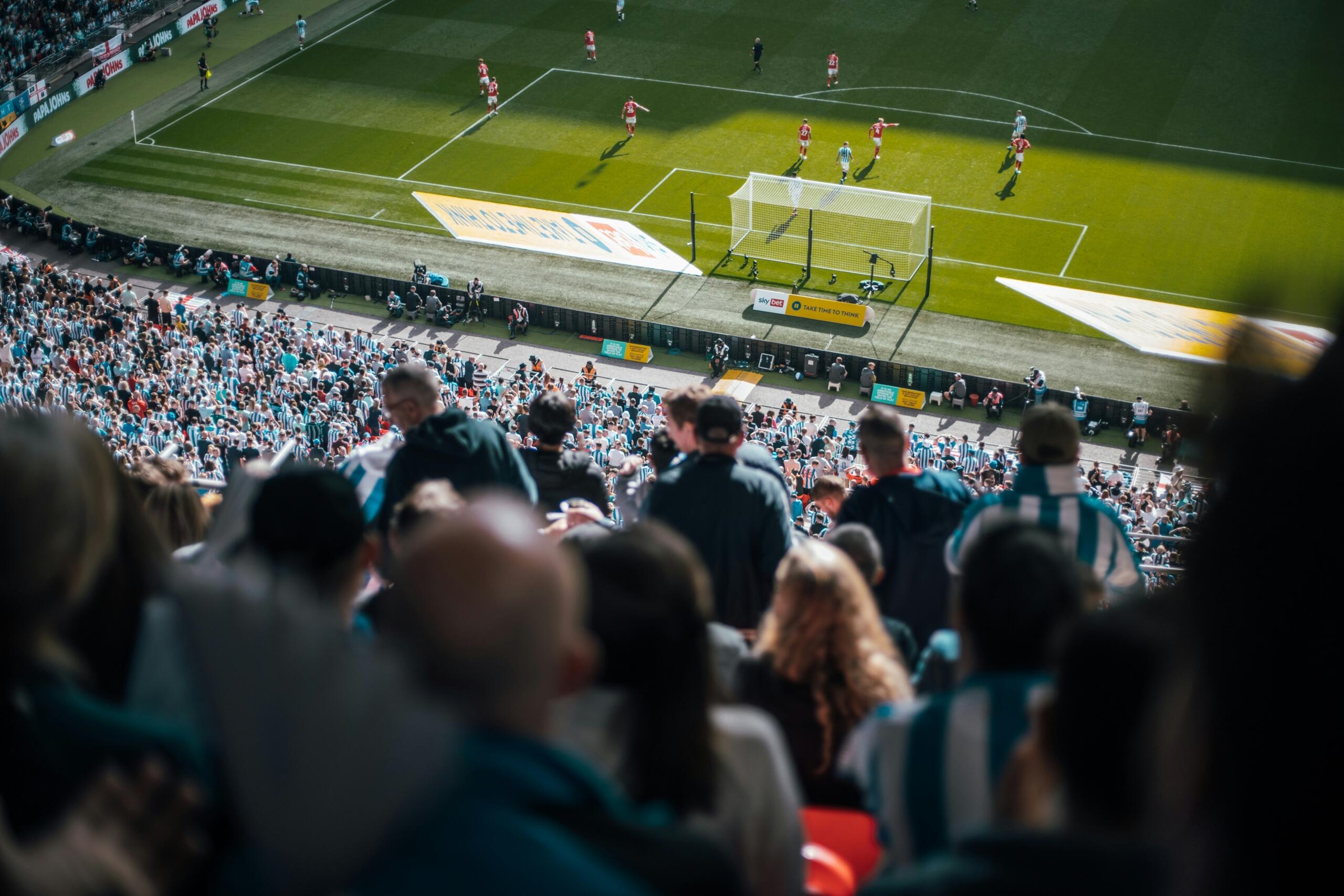 Supporters kijken vanaf de tribunes naar een voetbalwedstrijd in een groot stadion.