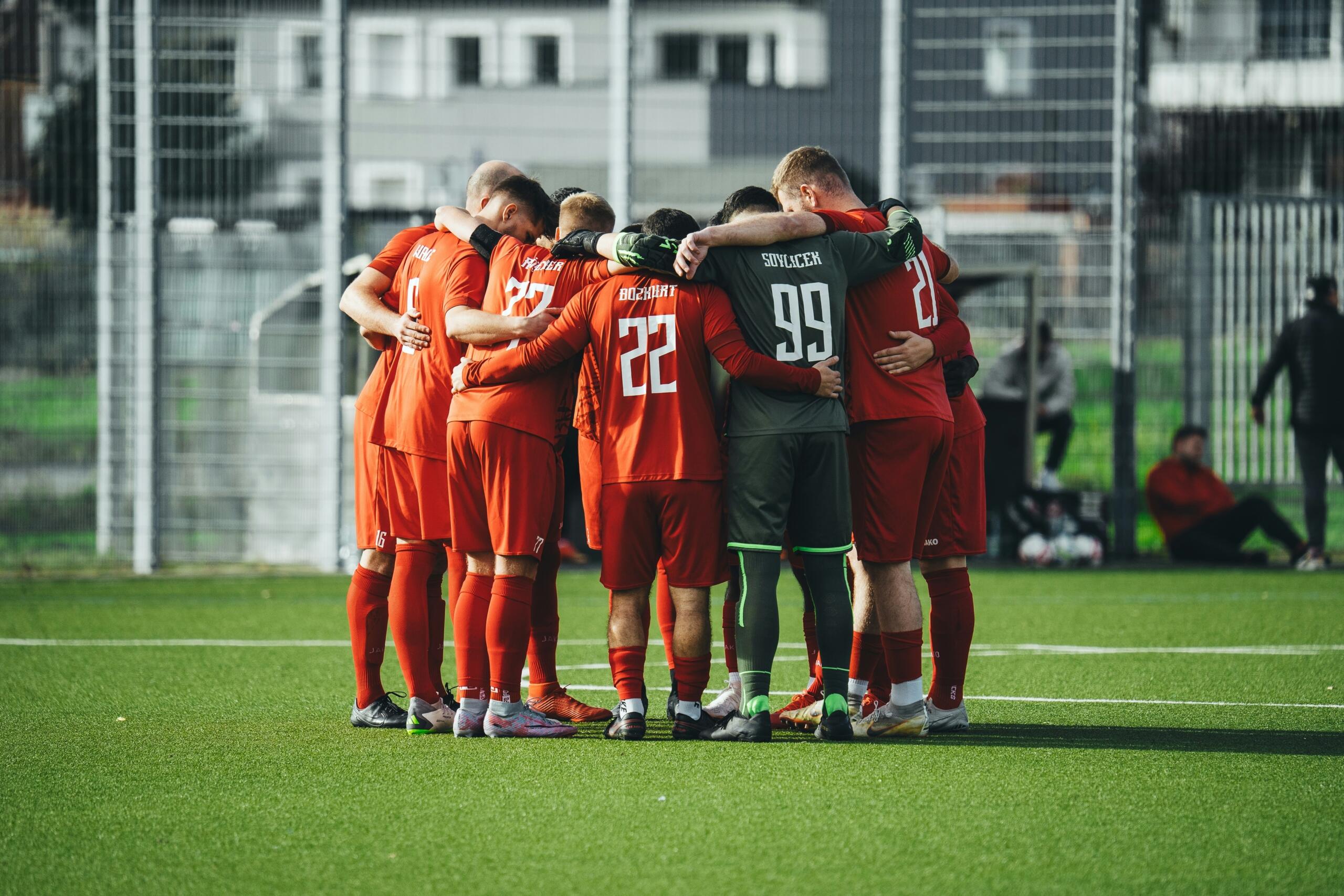 Een groep voetballers staat in een kring op het veld.