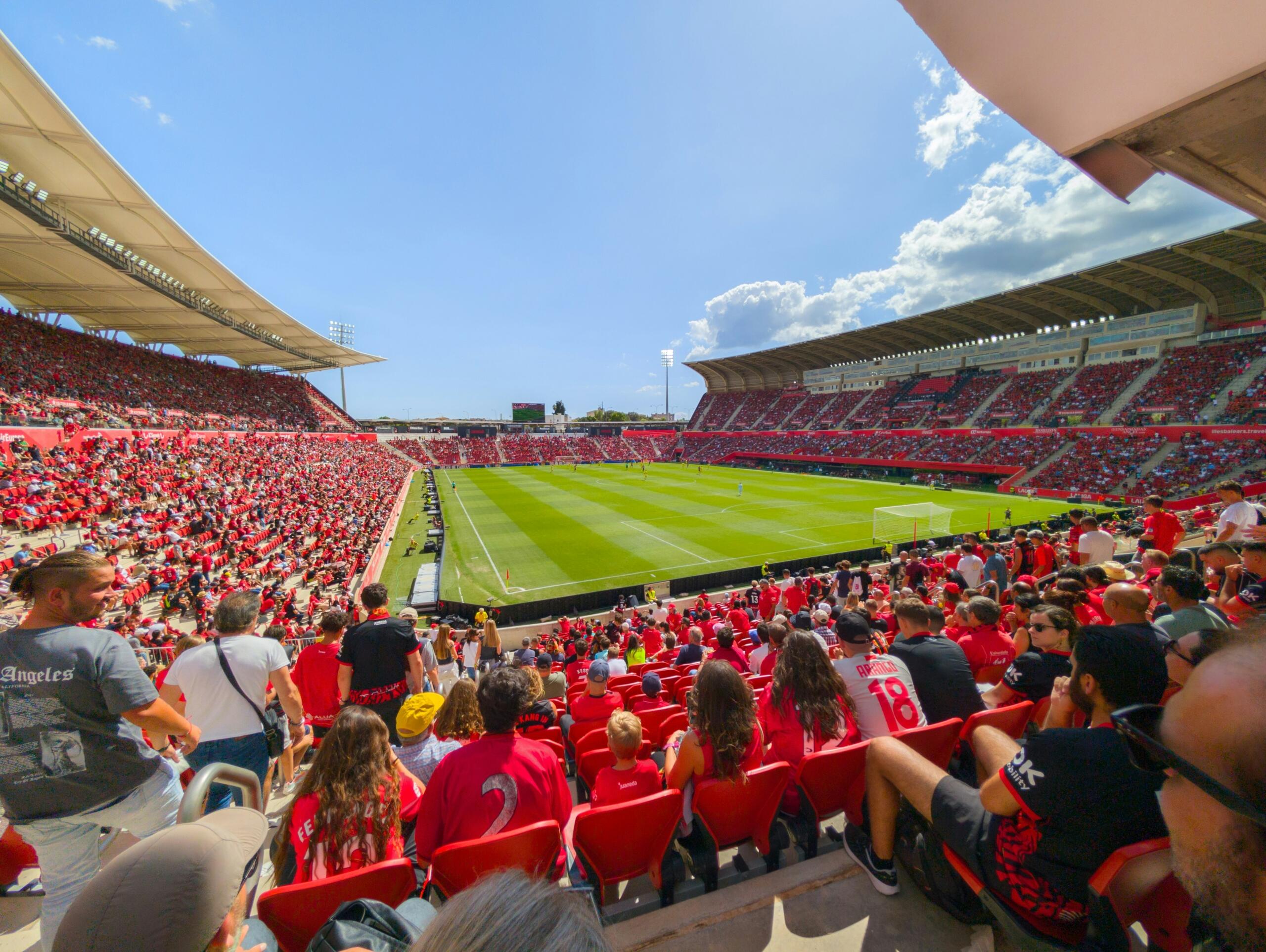 Supporters kijken vanaf de tribunes naar een voetbalwedstrijd in een vol stadion.