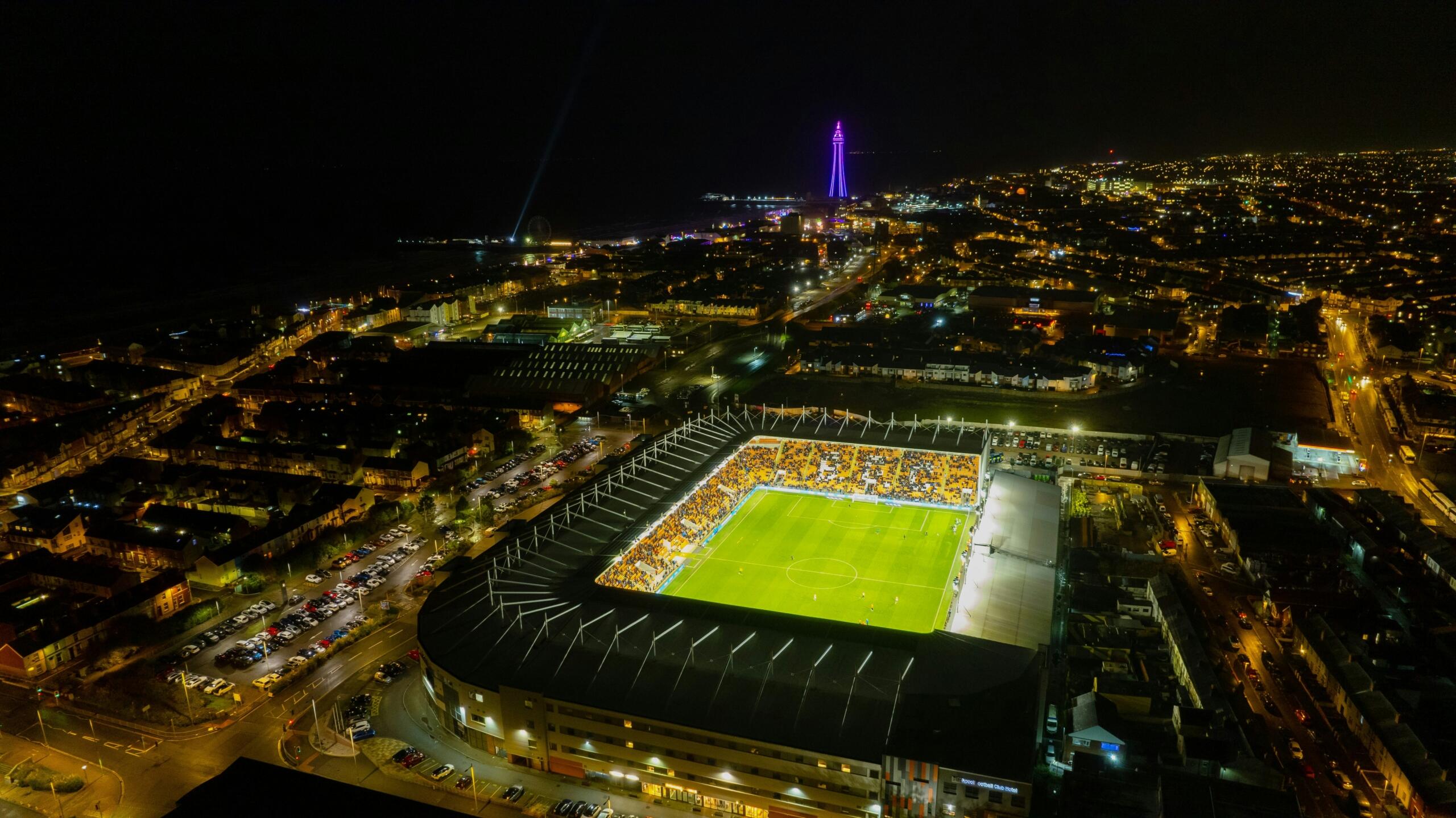 Luchtfoto van een verlicht voetbalstadion in de avond, gezien van bovenaf.