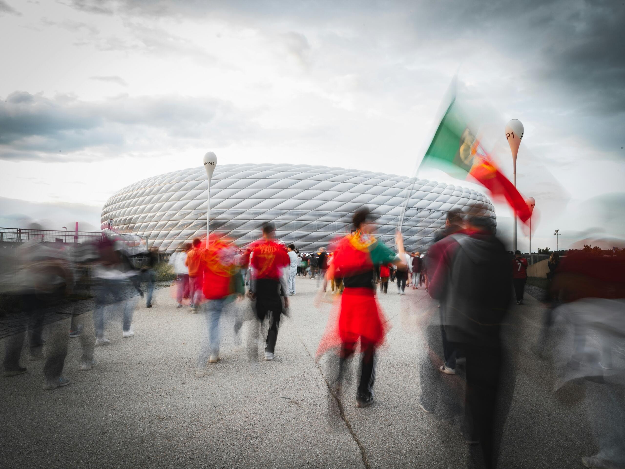 Mensen lopen bij een stadion terwijl iemand een vlag vasthoudt.