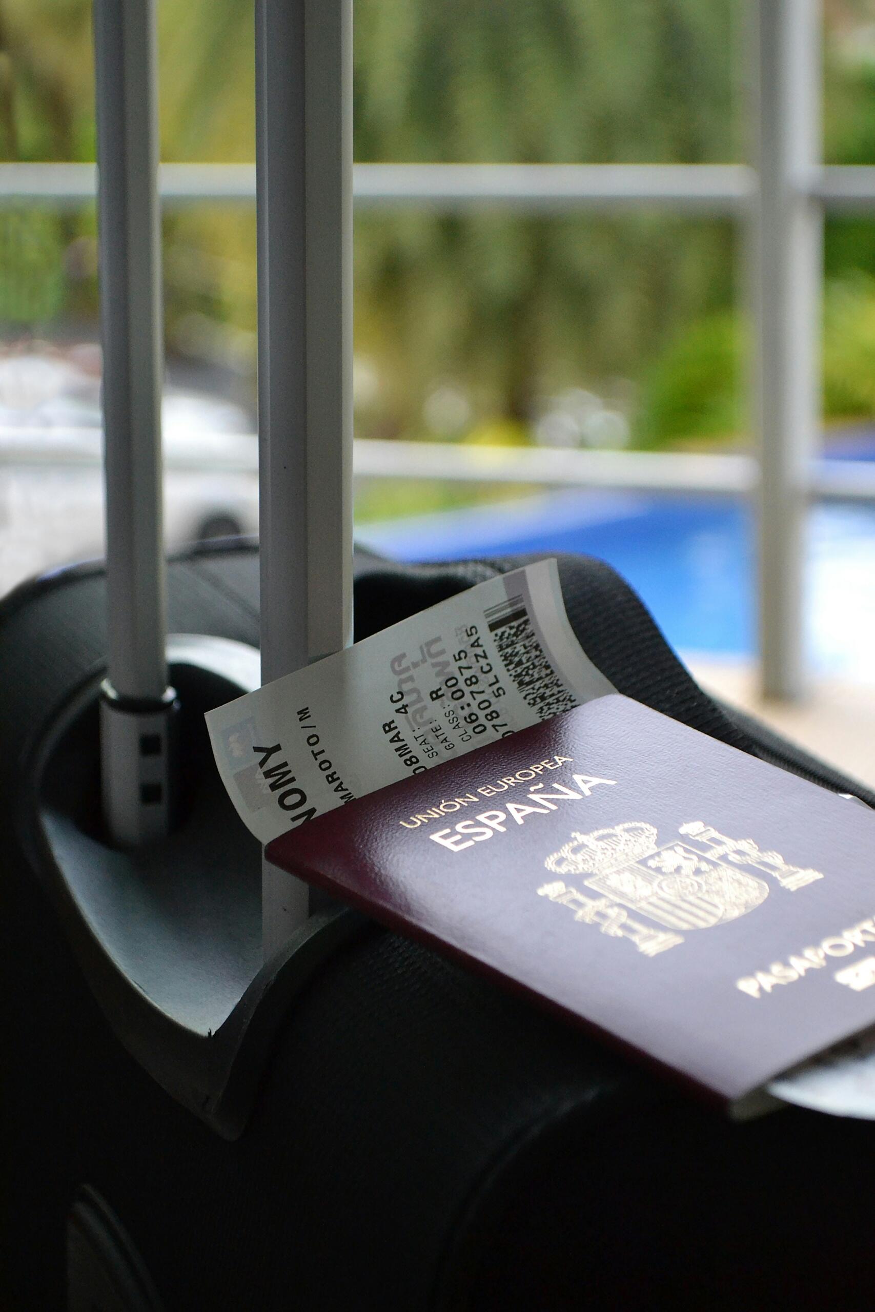 Een zwarte koffer staat naast een balkon, met een paspoort en boardingpass erop.