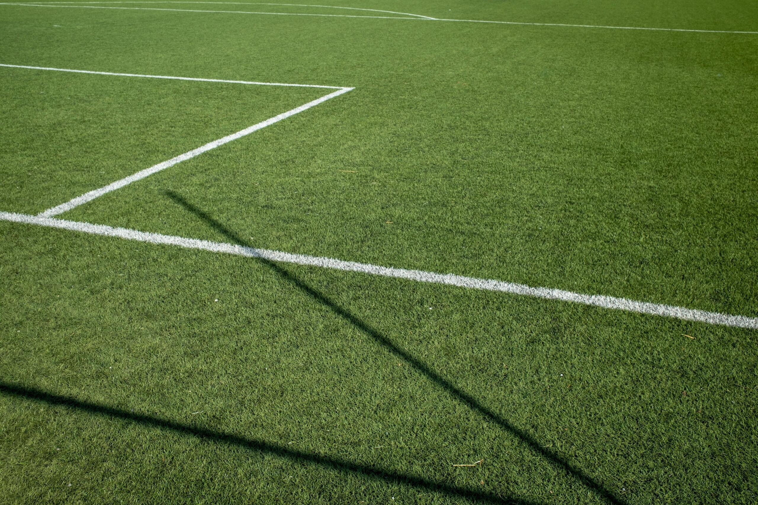 Een wit lijnstuk ligt over groen gras op een voetbalveld.