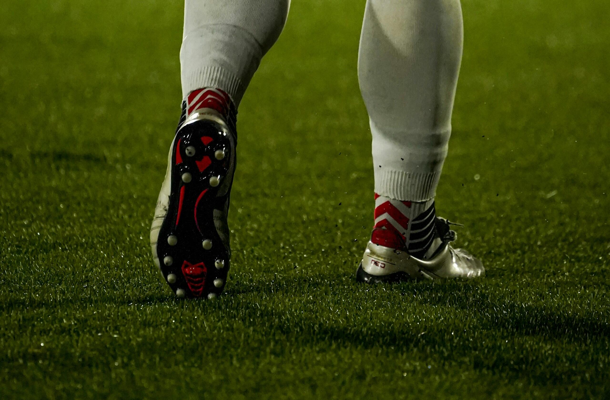 Voetballersbenen met voetbalschoenen staan op het gras.