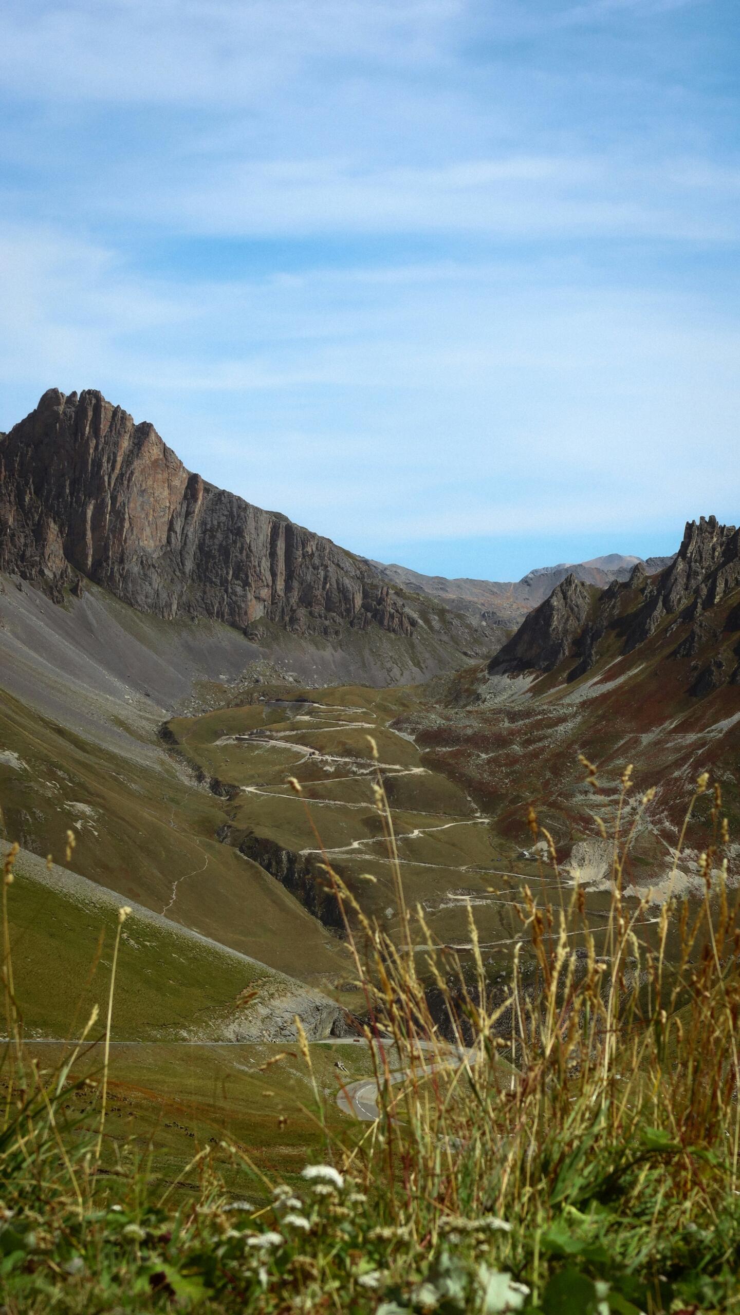 Een kronkelende bergweg loopt door een vallei met hoge bergen op de achtergrond.