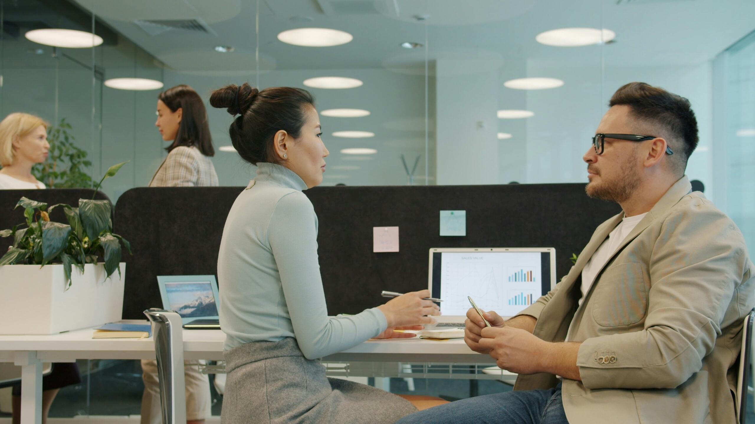 Twee collega’s zitten aan bureaus in een kantoor en bespreken werk met elkaar.