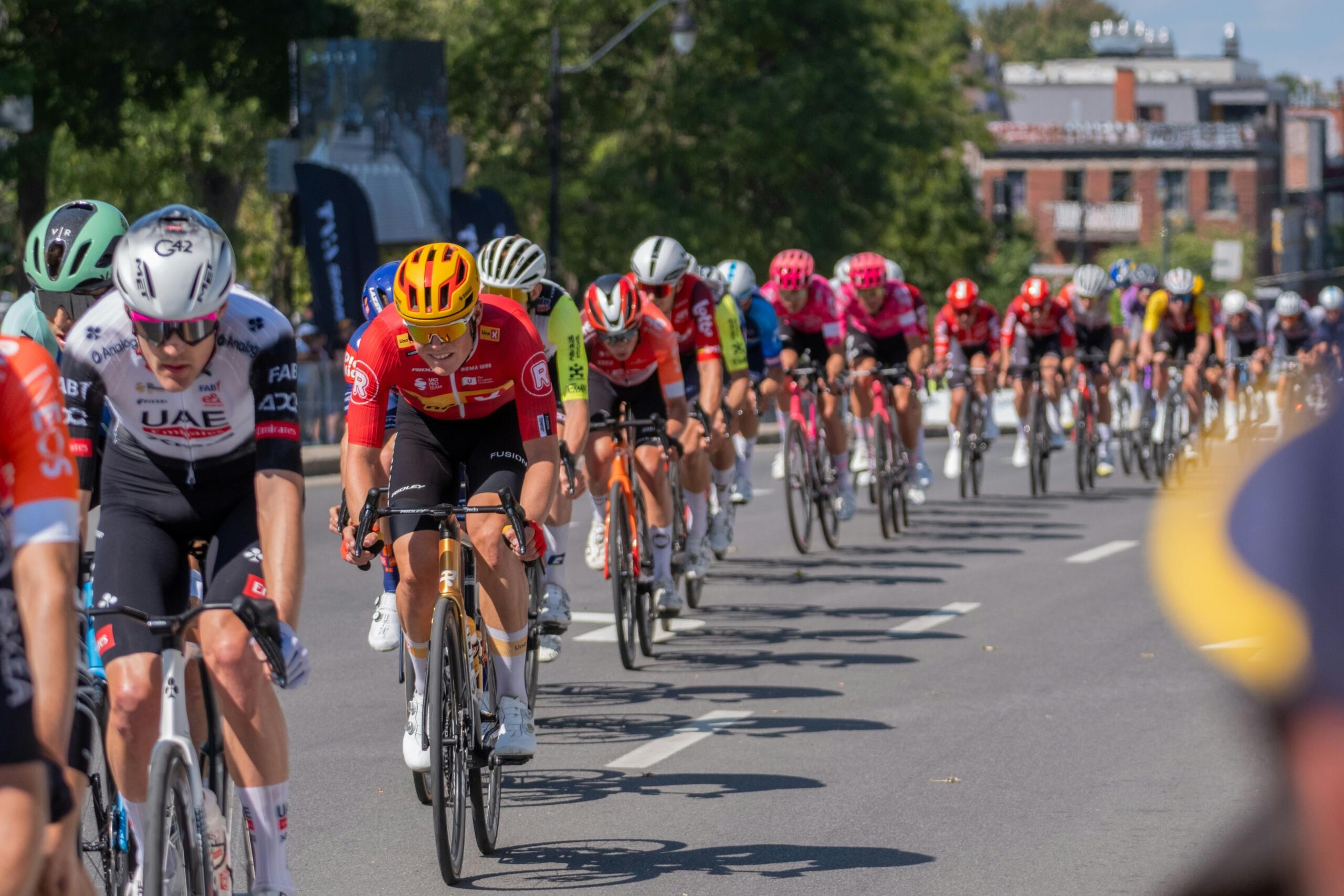 Wielrenners rijden dicht bij elkaar in een peloton op een zonnige dag.