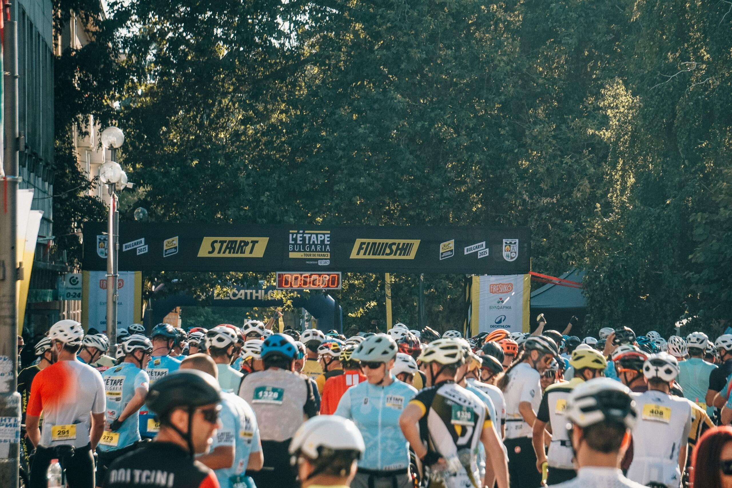Een grote groep wielrenners staat verzameld bij een start- of finishzone.