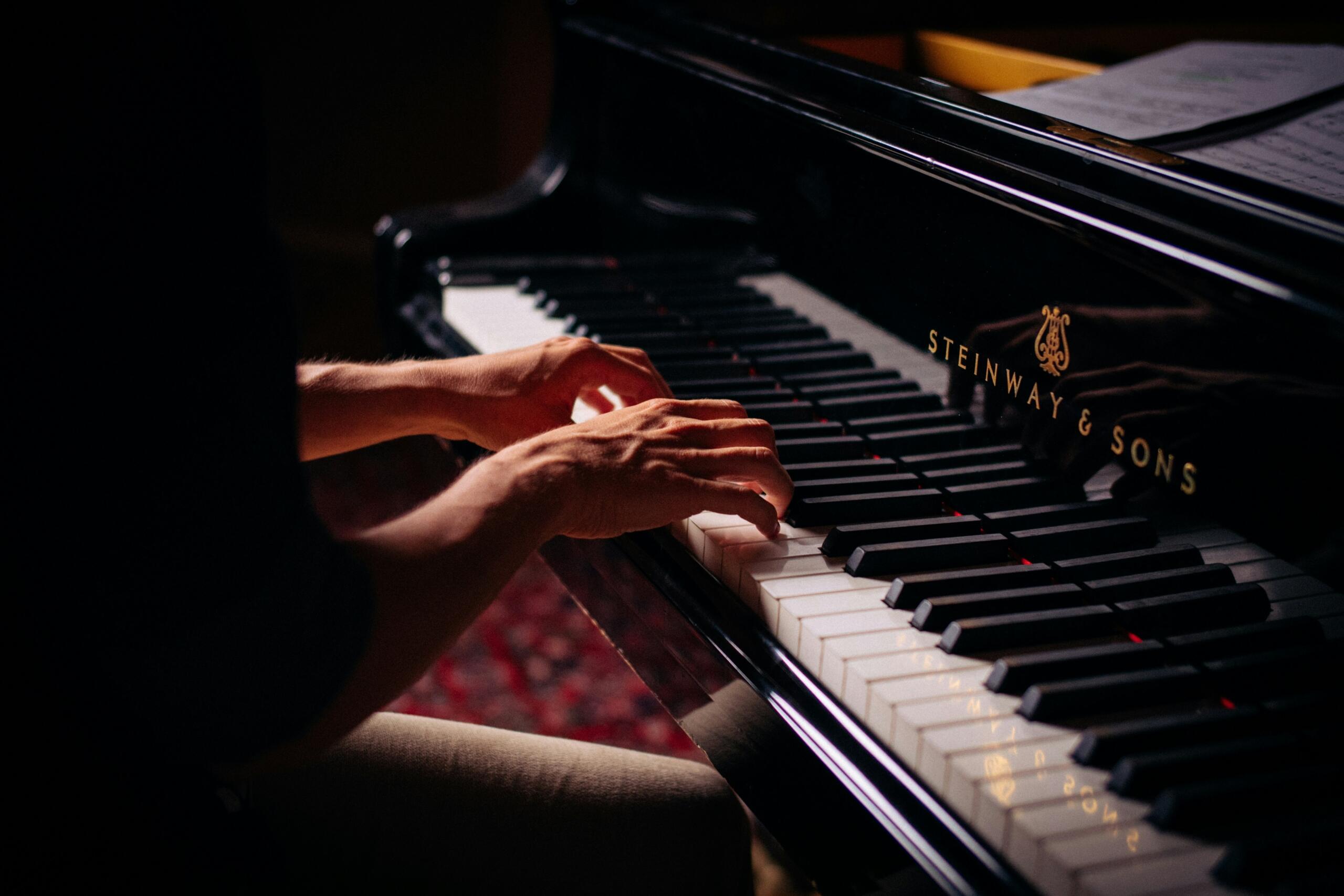 Handen spelen op de toetsen van een zwarte Steinway & Sons-piano.