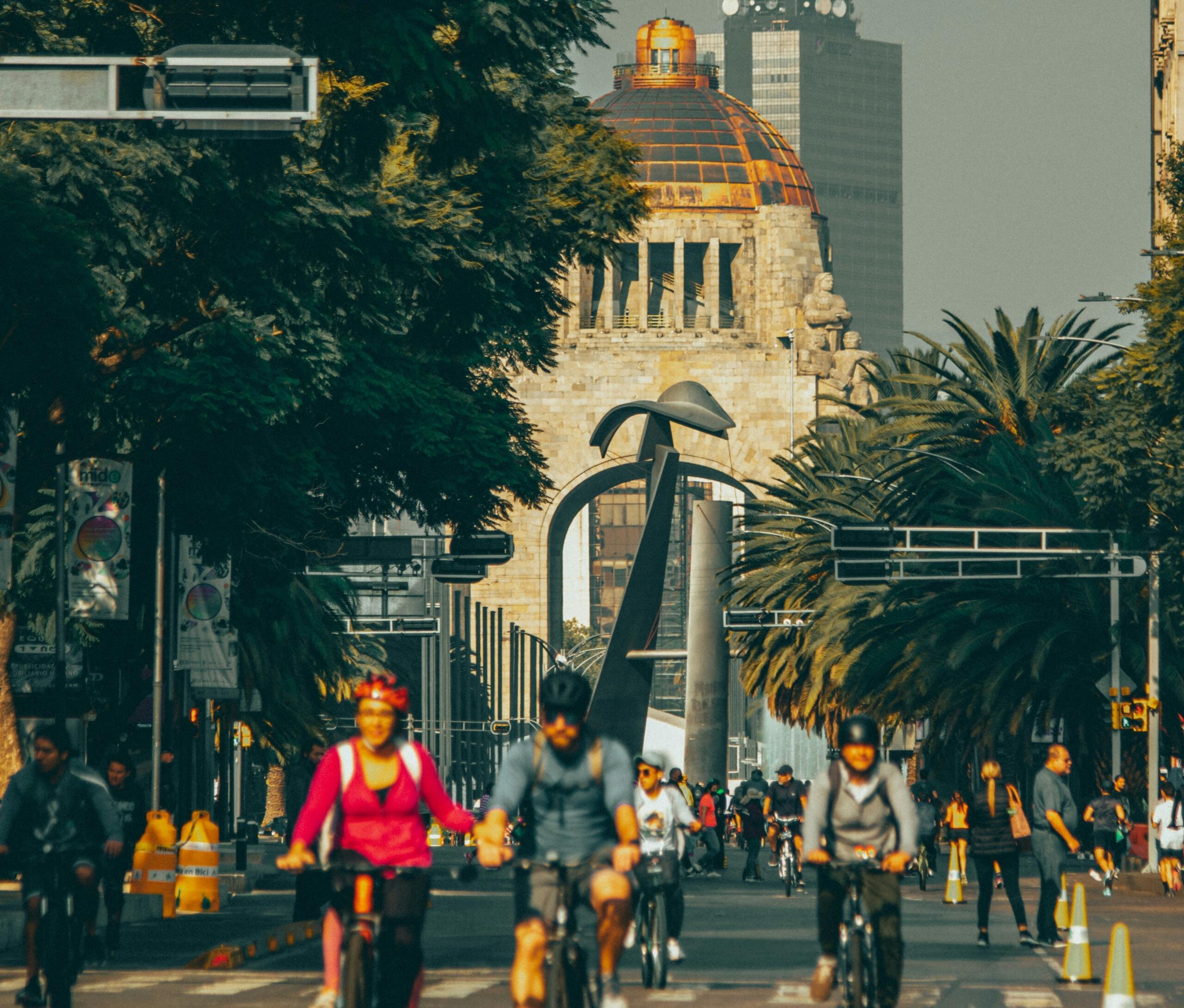 Drukke straat in Mexico-Stad met fietsers, palmbomen en een historisch gebouw op de achtergrond | Bron: Roger Ce, via Unsplash