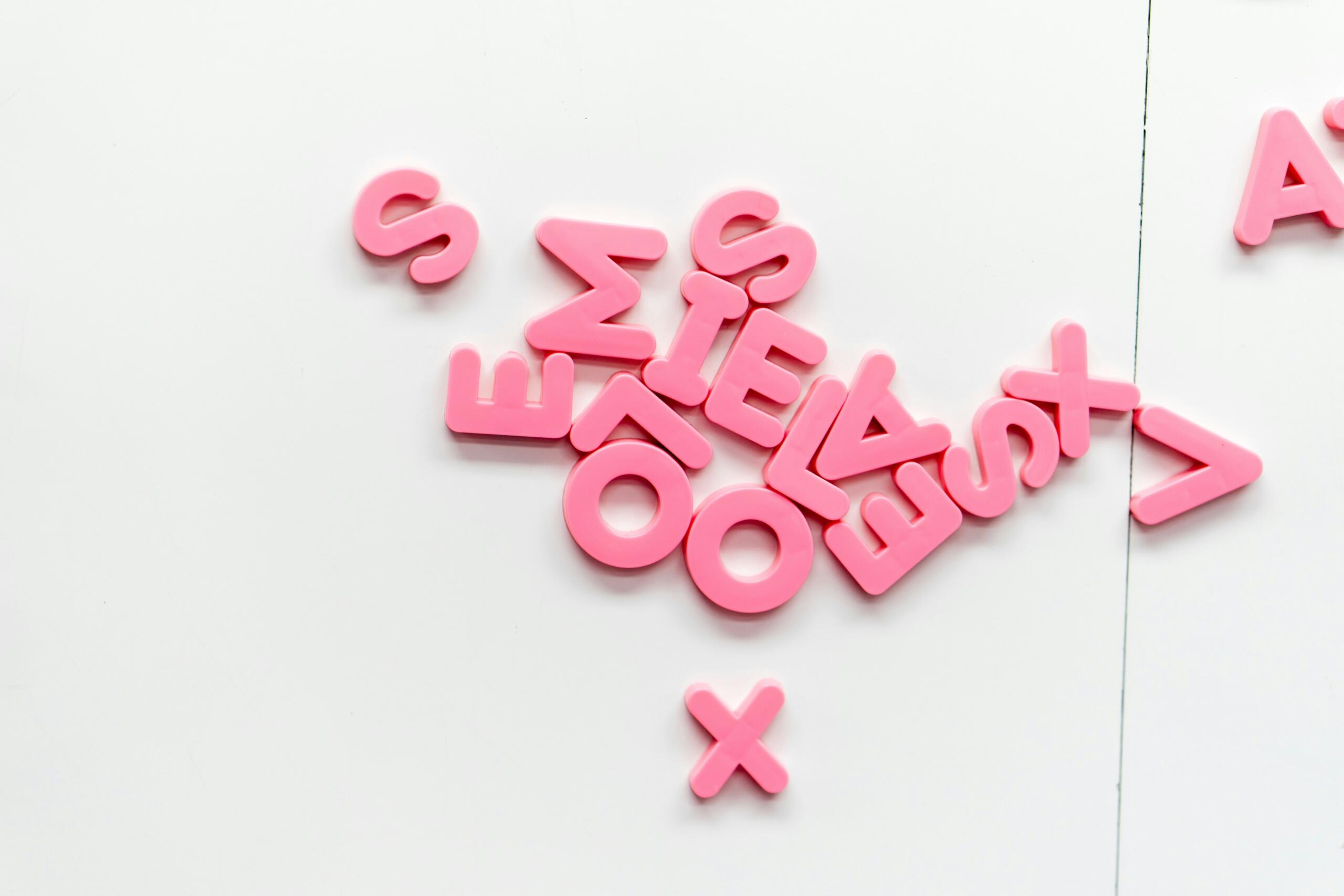 Roze kunststof letters liggen verspreid op een witte ondergrond.