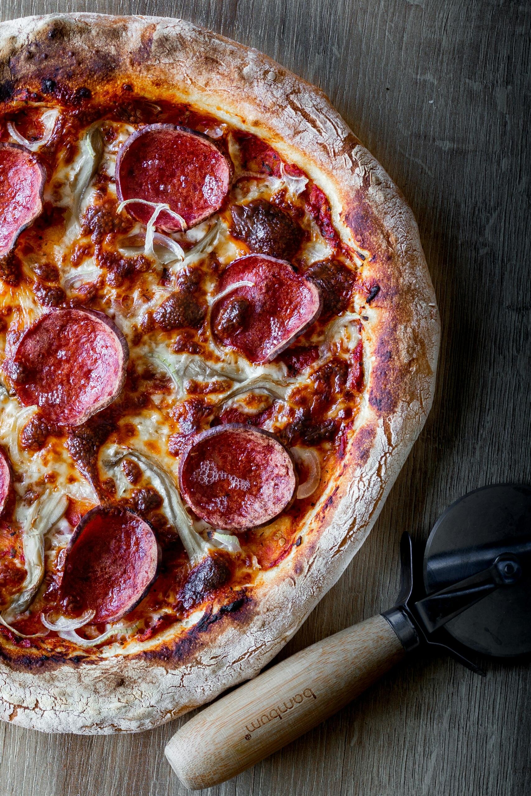 Pepperoni pizza met gesmolten kaas en pizzasnijder op tafel | Bron: Sahand Hoseini