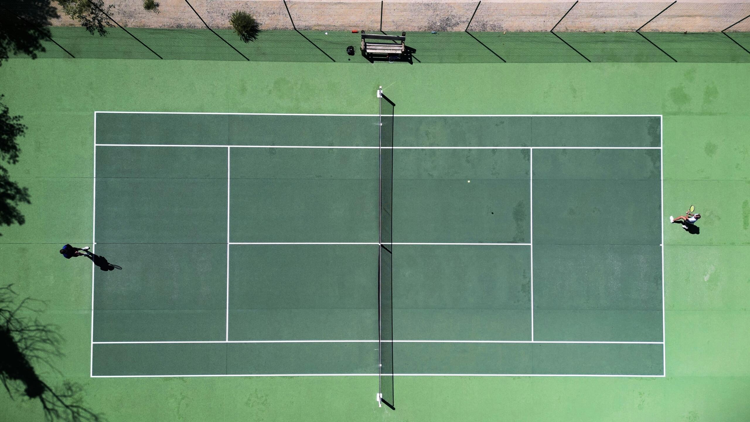 Twee spelers spelen een tenniswedstrijd op een groene baan, gezien van bovenaf | Bron: Julius Hildebrandt, via Unsplash