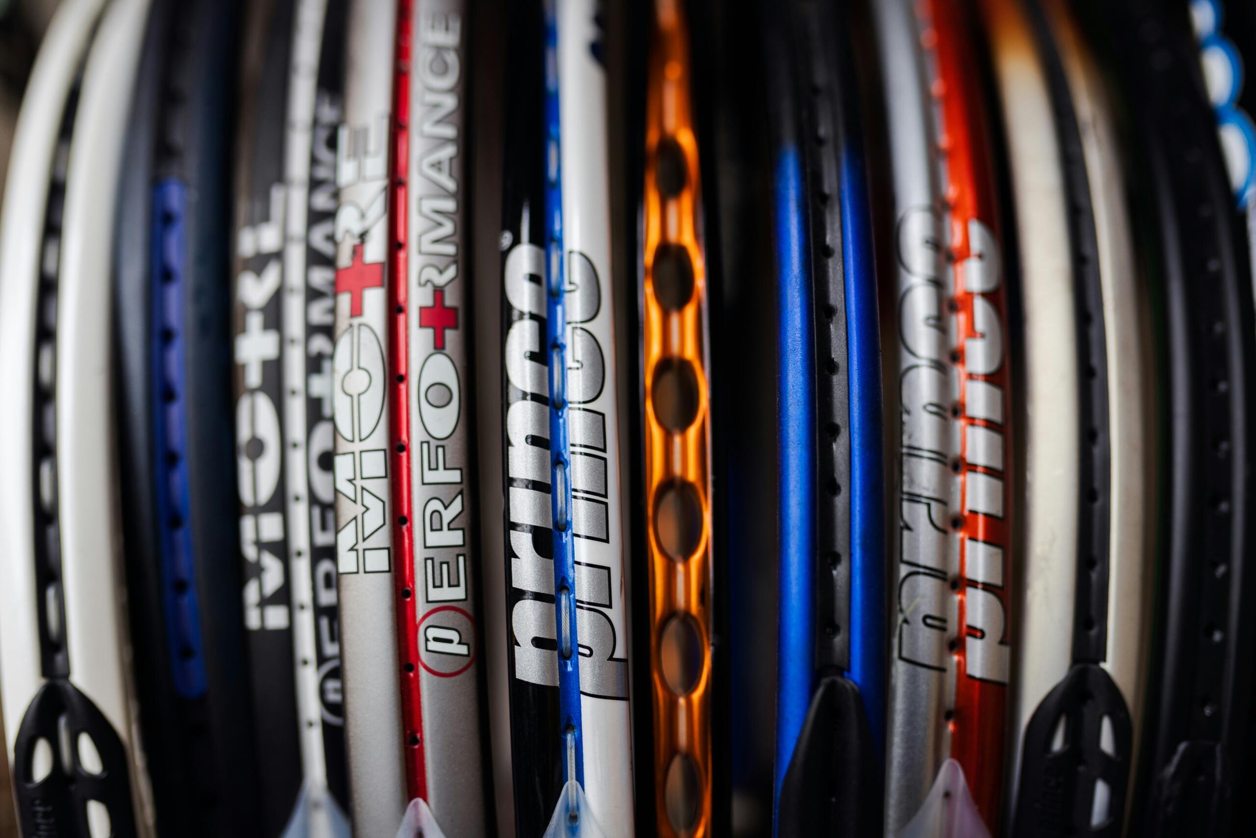 Een rij tennisrackets staat naast elkaar, met verschillende kleuren en frameprofielen zichtbaar.