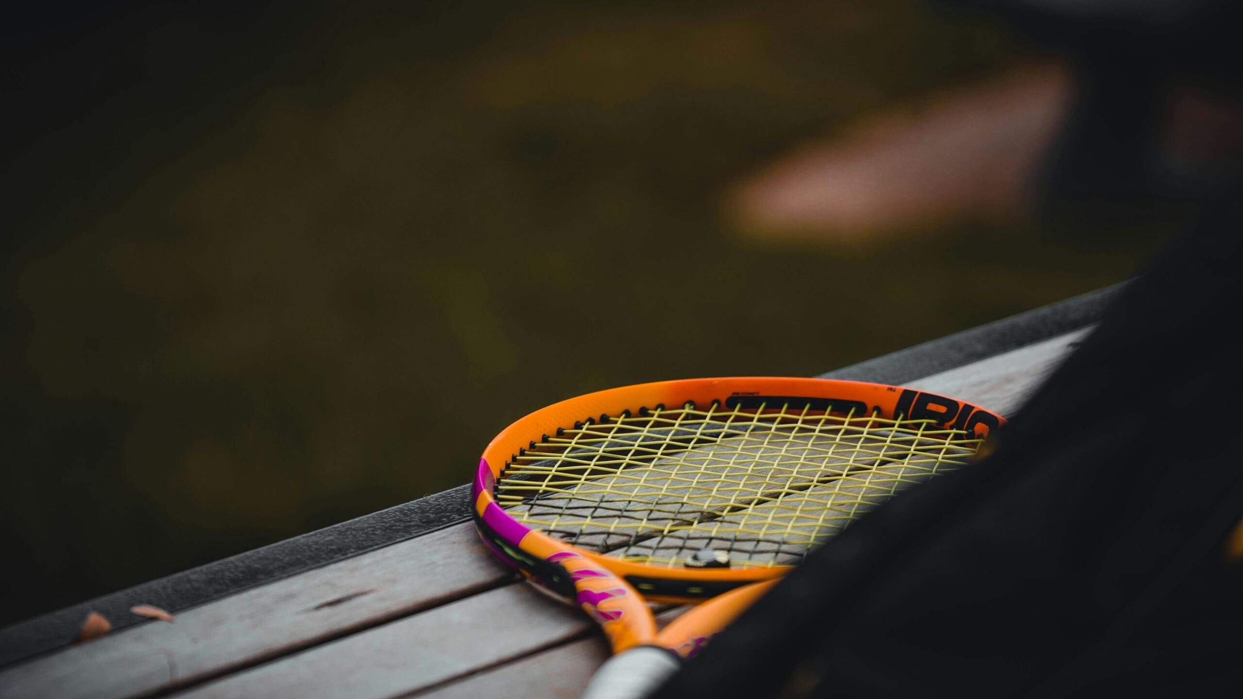 Een oranje tennisracket ligt op een houten bank.