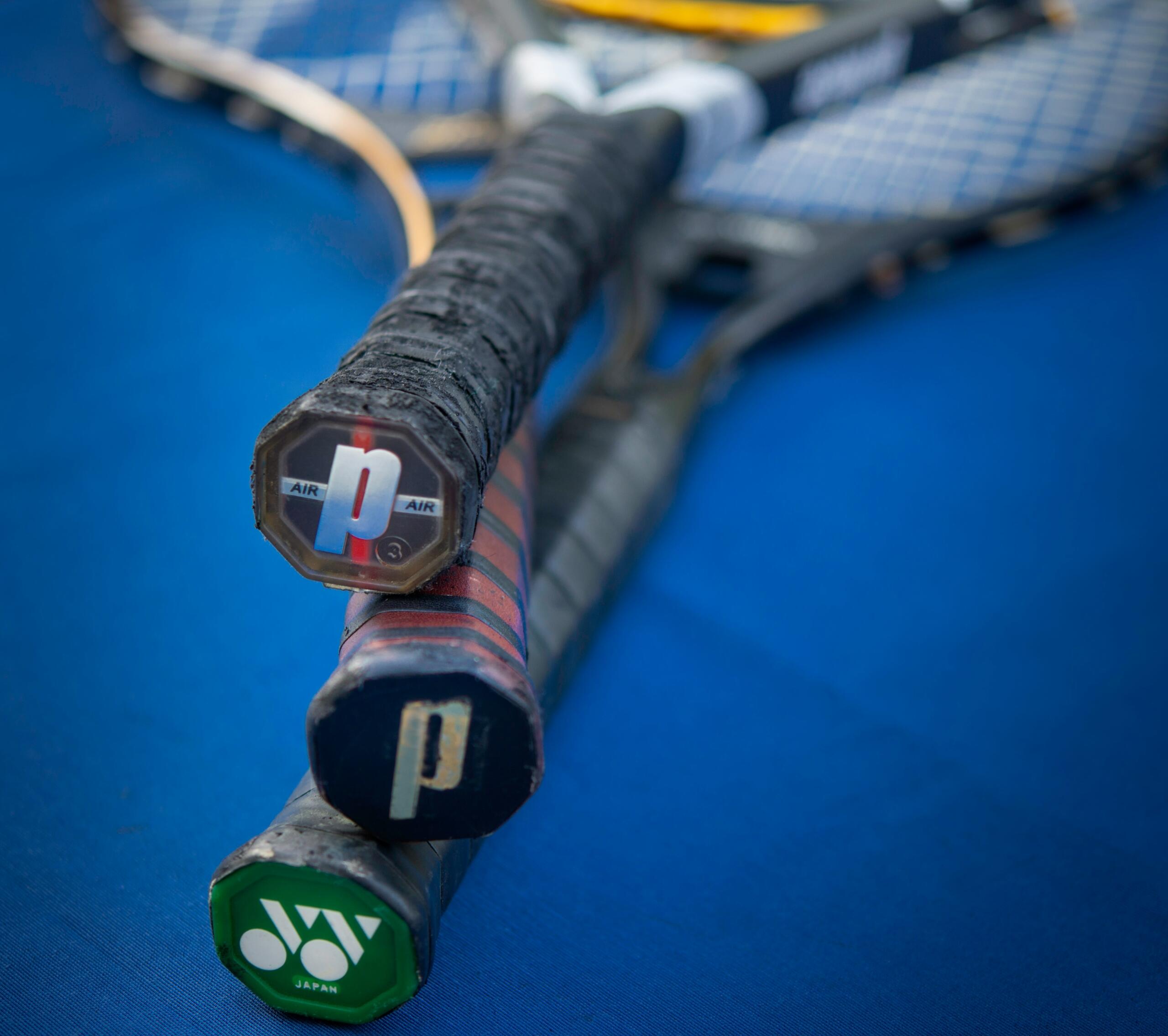 Meerdere tennisrackets liggen op een blauwe ondergrond, met de handvatten dicht bij de camera.