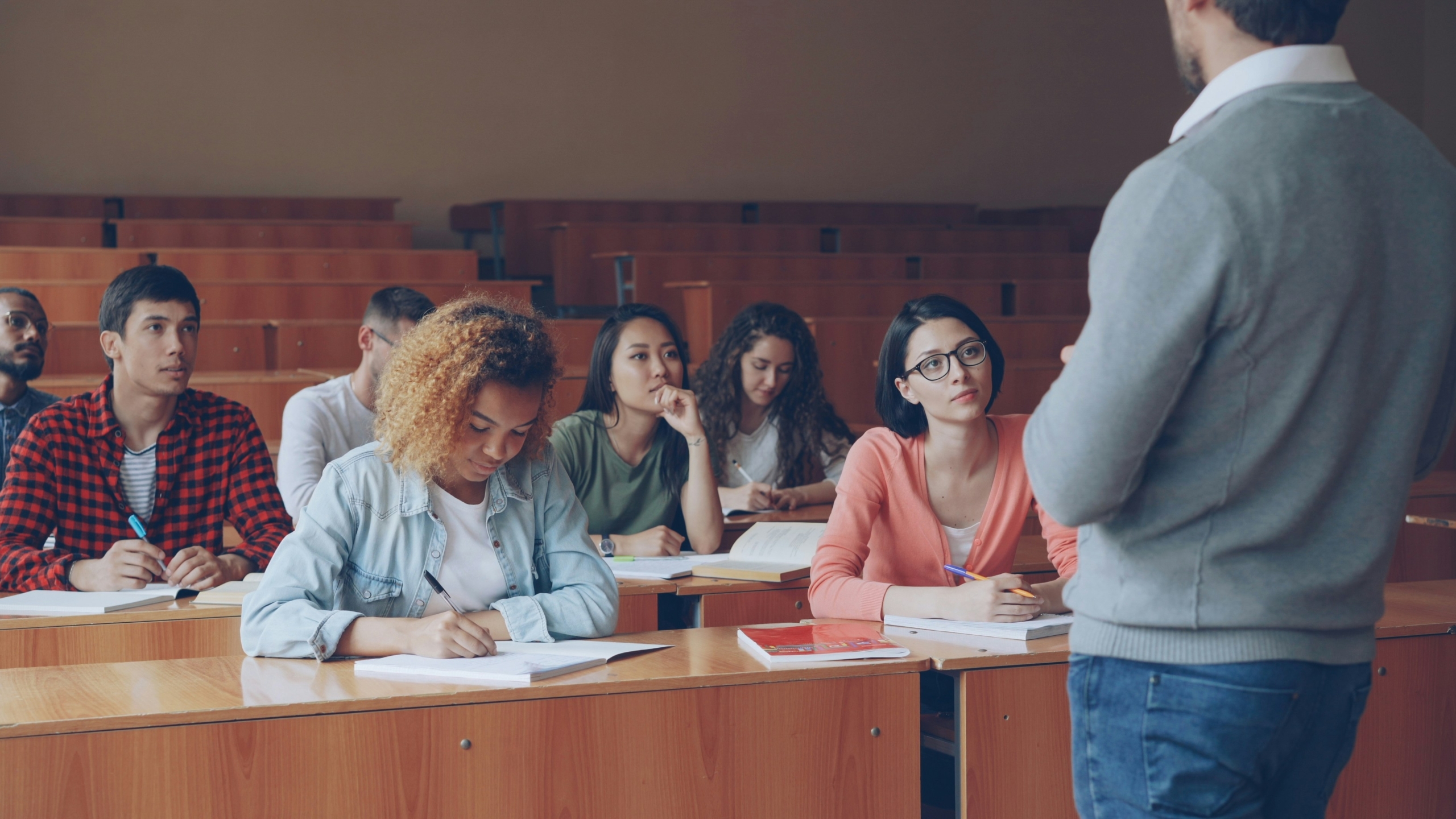 Een docent staat voor een collegezaal met studenten die aan tafels zitten.