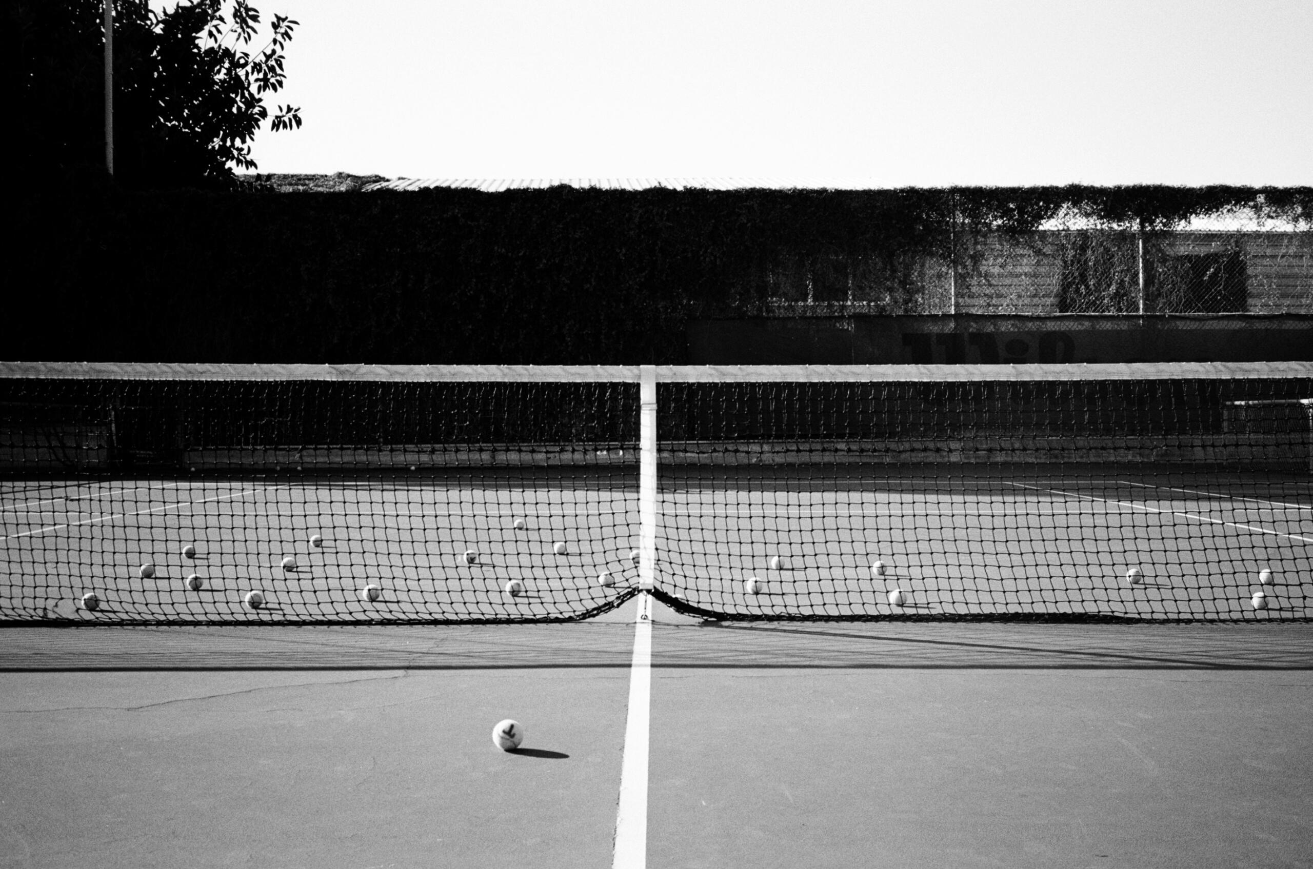 Een zwart-witfoto van een tennisnet met meerdere tennisballen verspreid over de baan.