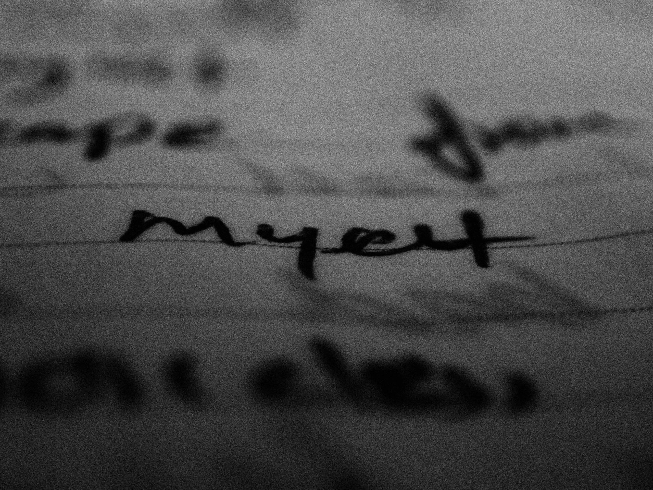 Close-up van handgeschreven woorden op gelinieerd papier, waarbij een deel van de tekst scherp in beeld is.