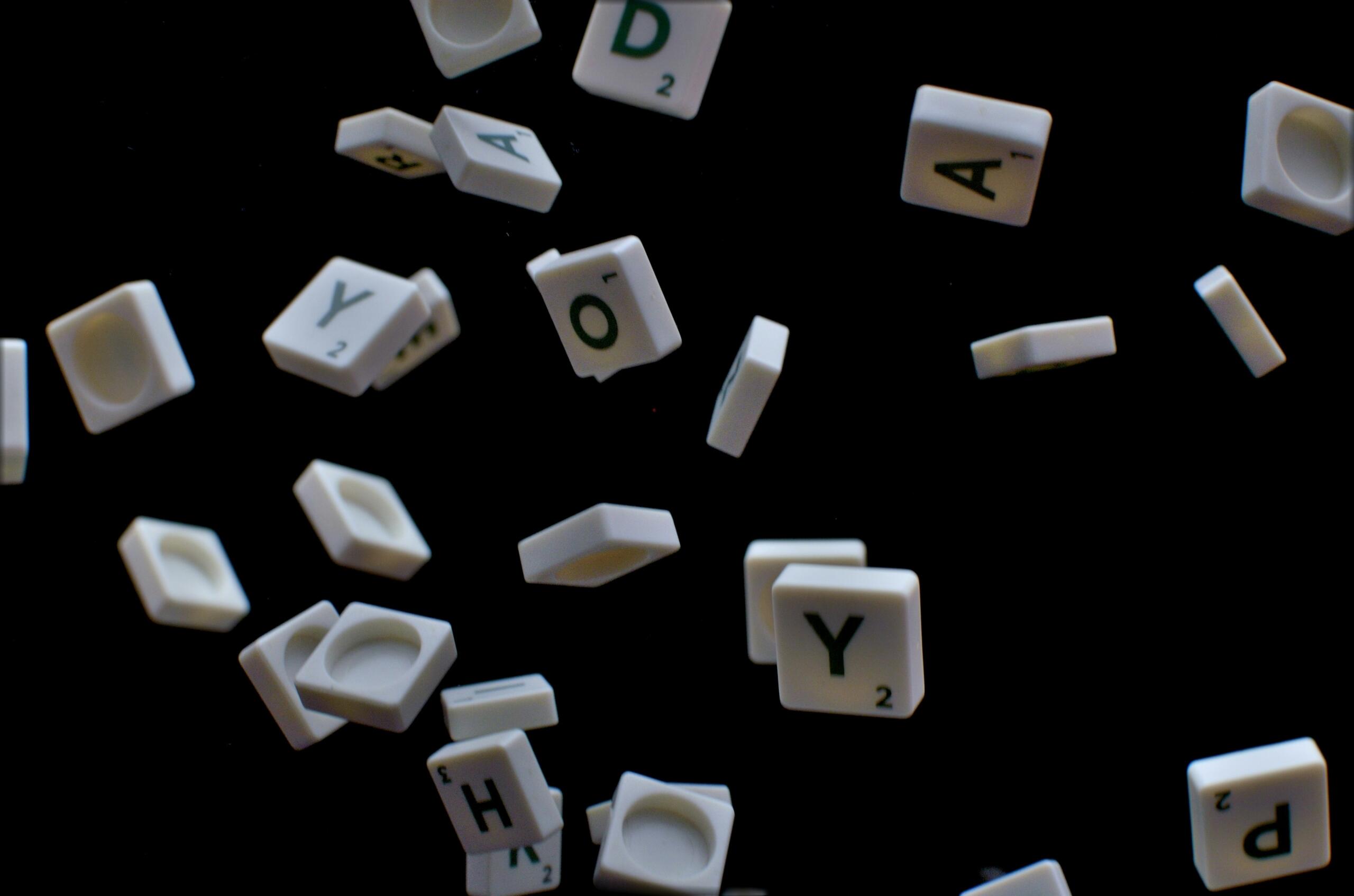Witte letterblokjes met zwarte letters liggen verspreid op een zwarte achtergrond.